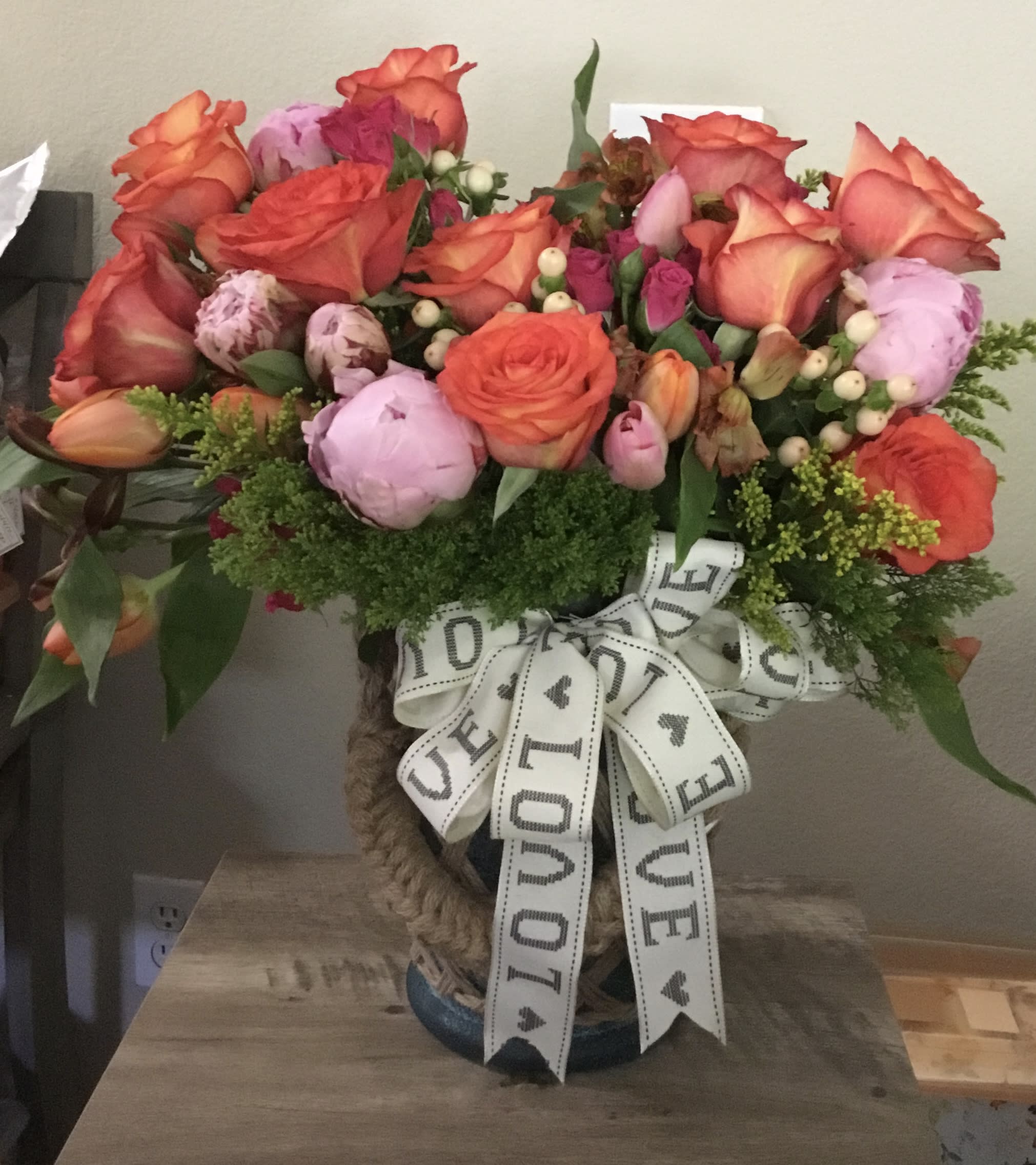 Bouquet of orange roses and pink peonies in a woven vase with a LOVE ribbon