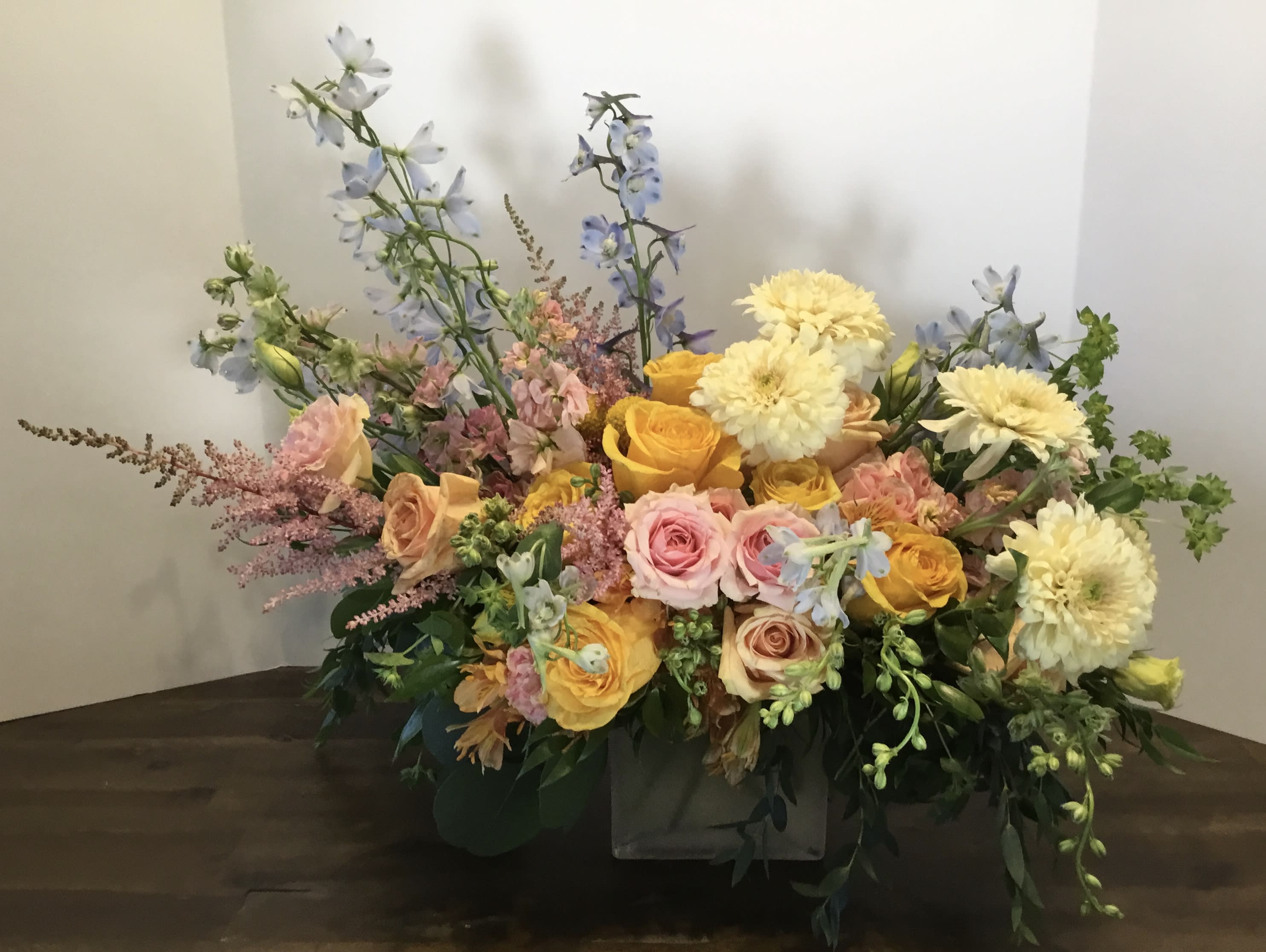 Mixed bouquet of roses, dahlias, and blue delphinium in a low container
