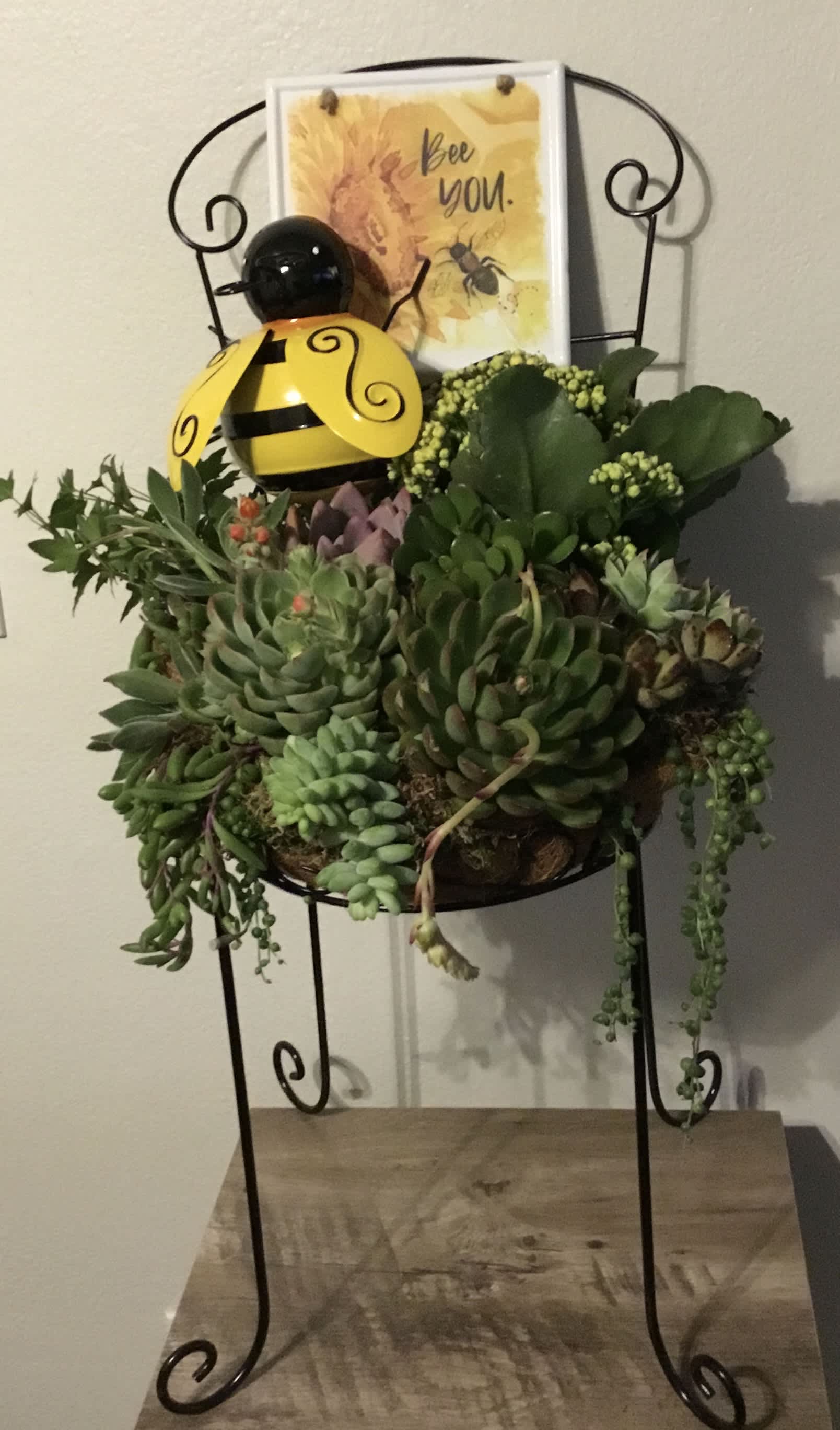 Succulent arrangement in a metal stand with a bee decoration and card
