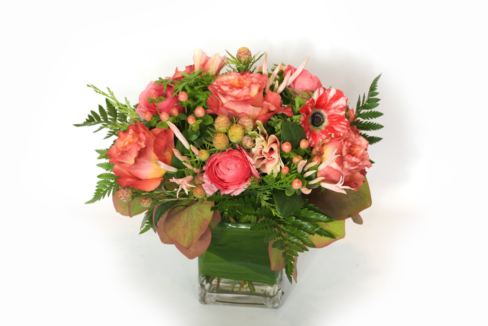Pink and coral flower arrangement in a clear square vase