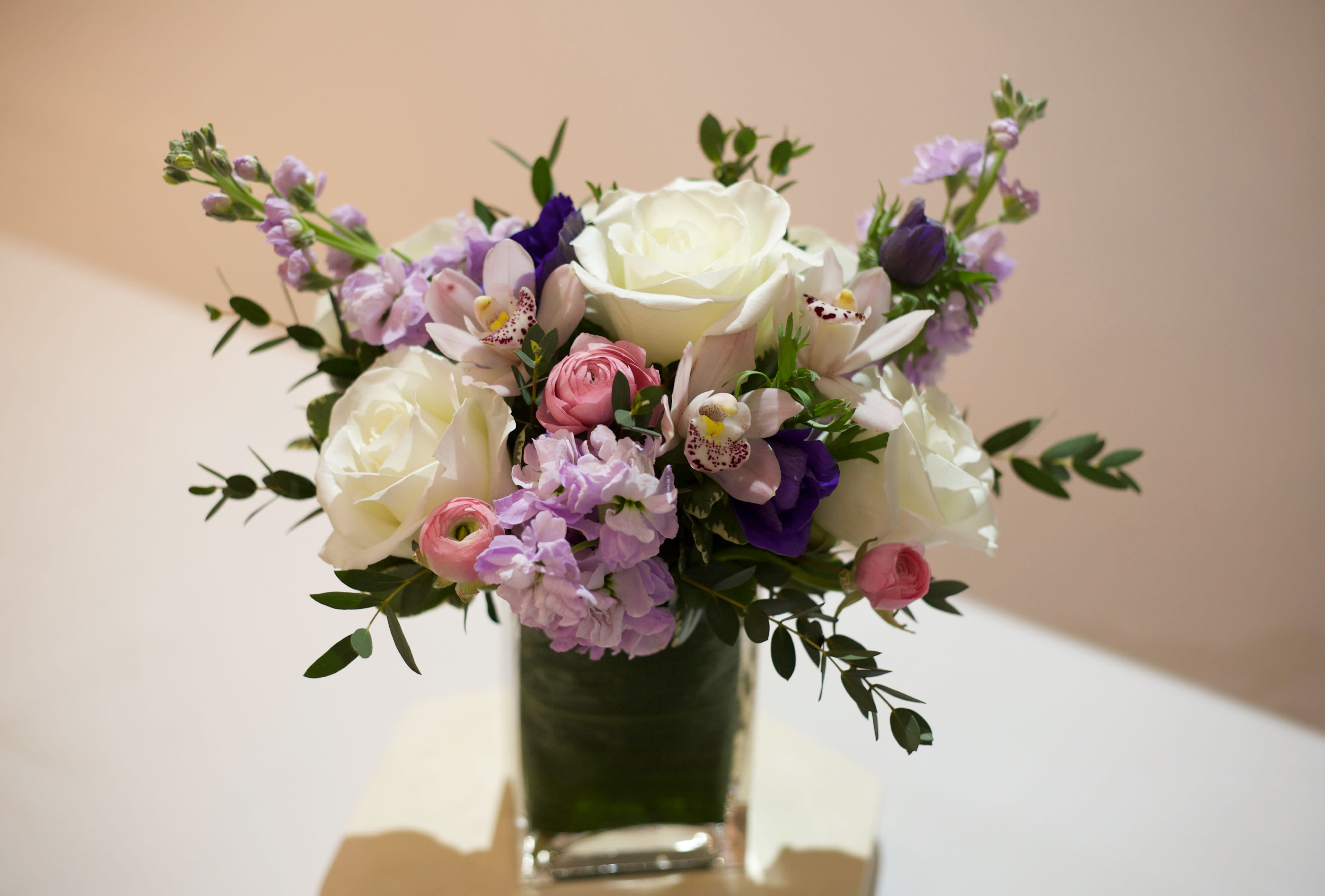 Bouquet of white roses, pink blooms, and purple flowers in a glass vase