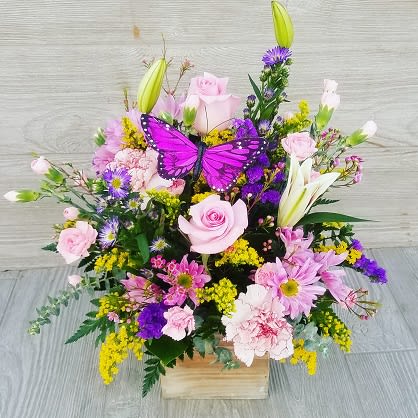 Pink and purple flower arrangement in a wooden box with a butterfly decoration