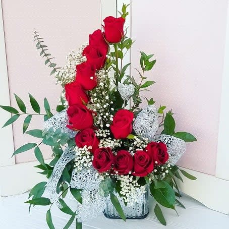 Tall and low arrangement of red roses with white filler flowers in a silver vase with white lace ribbon
