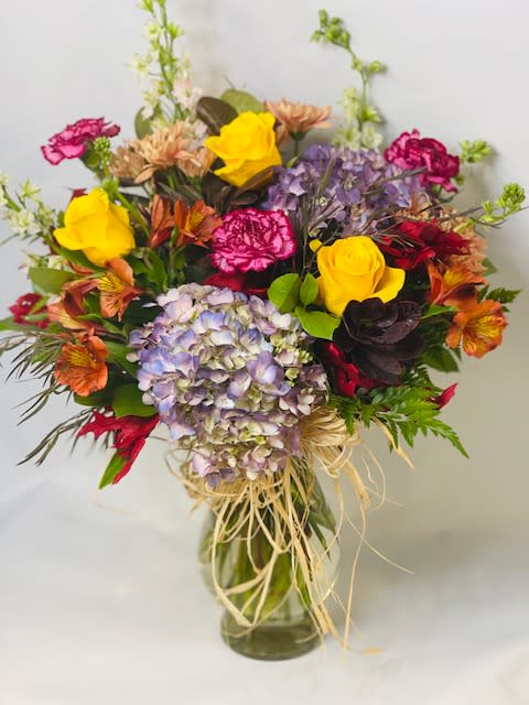 Mixed bouquet of roses, hydrangeas, and carnations in a glass vase