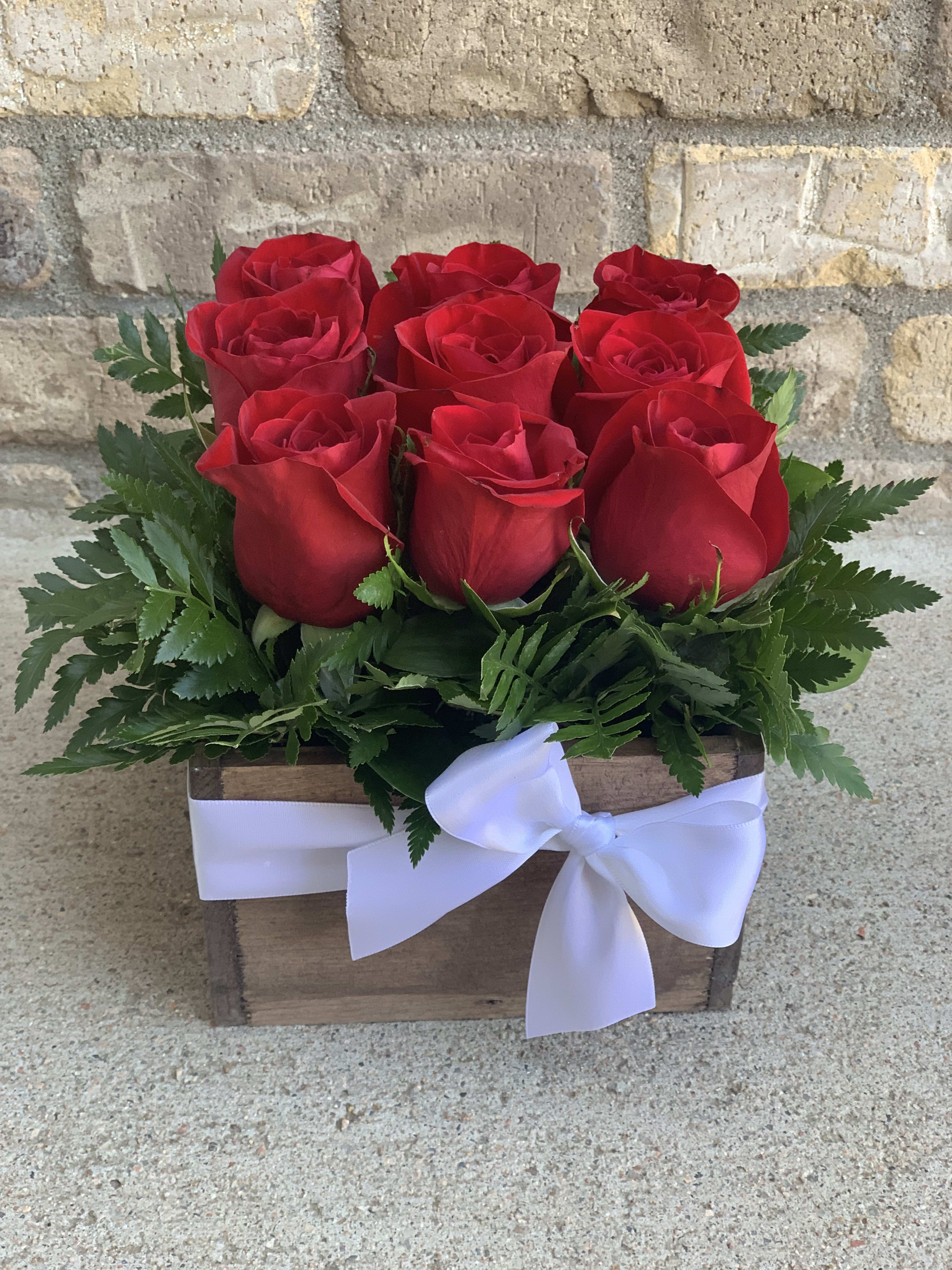 Red roses arranged in a wooden box with a white ribbon