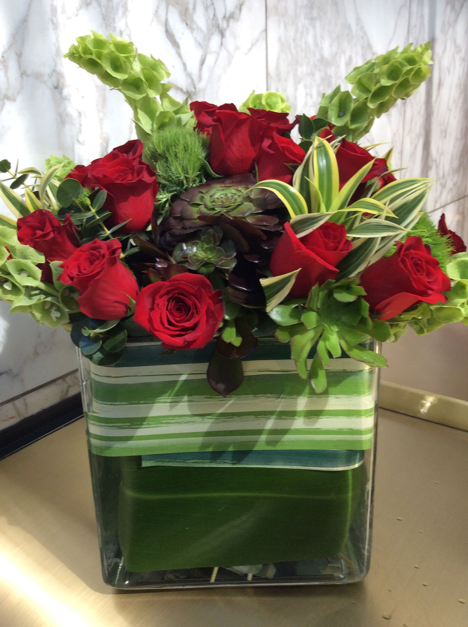 Red roses in a square glass vase with green succulents