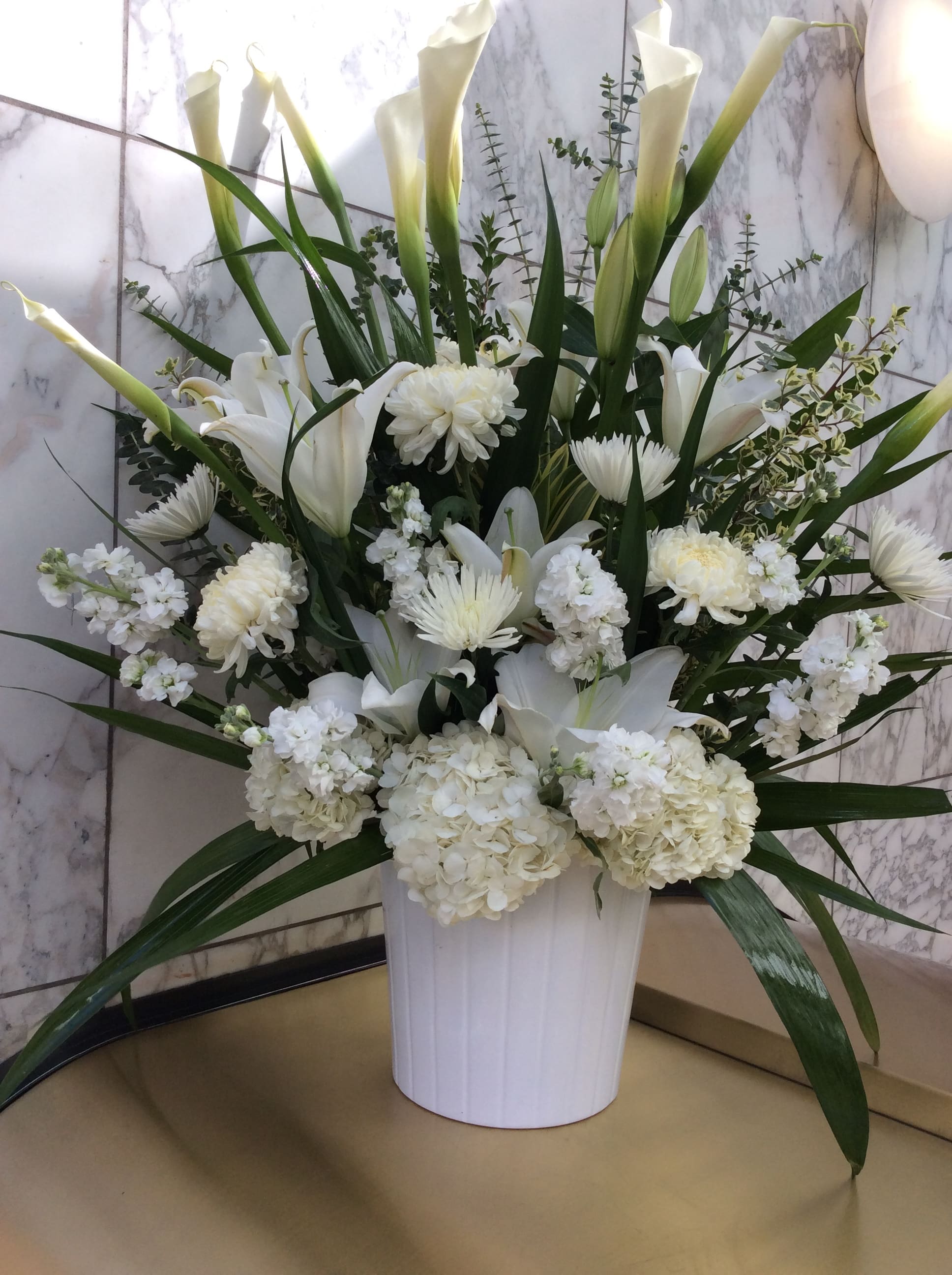 White floral arrangement in a white vase with tall calla lilies and chrysanthemums