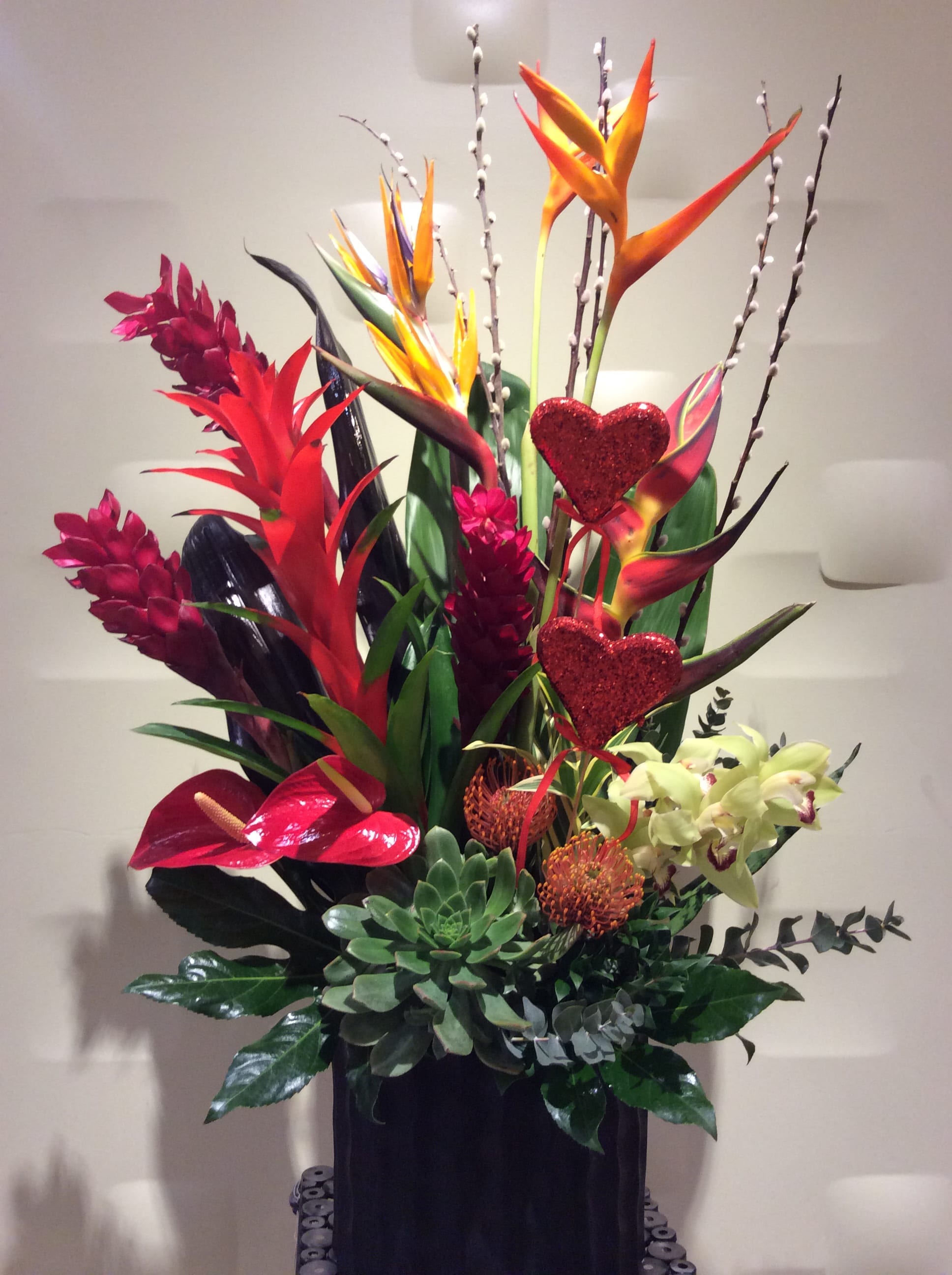 Tall tropical arrangement with red and orange blooms in a black container