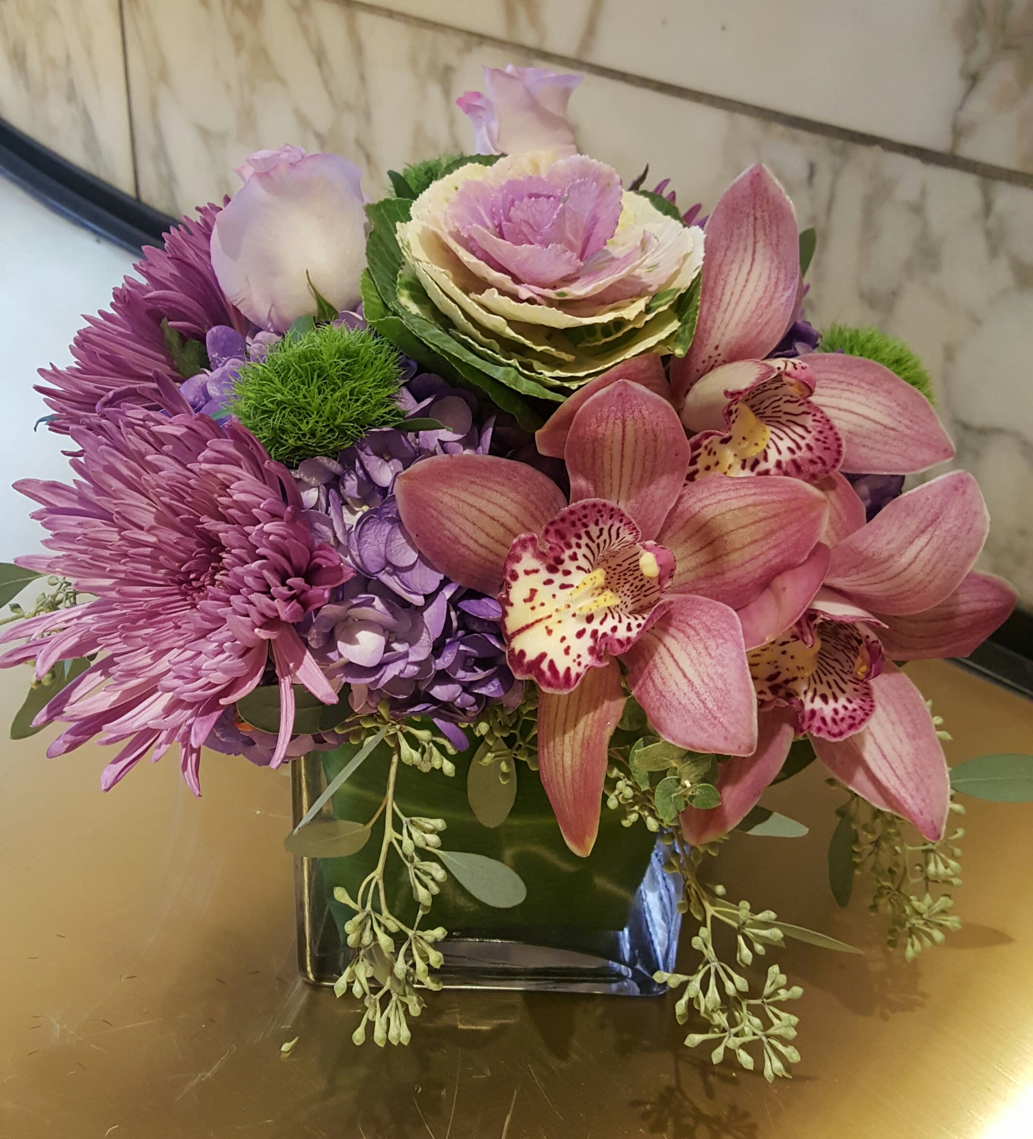 Purple and pink floral arrangement in a square glass vase