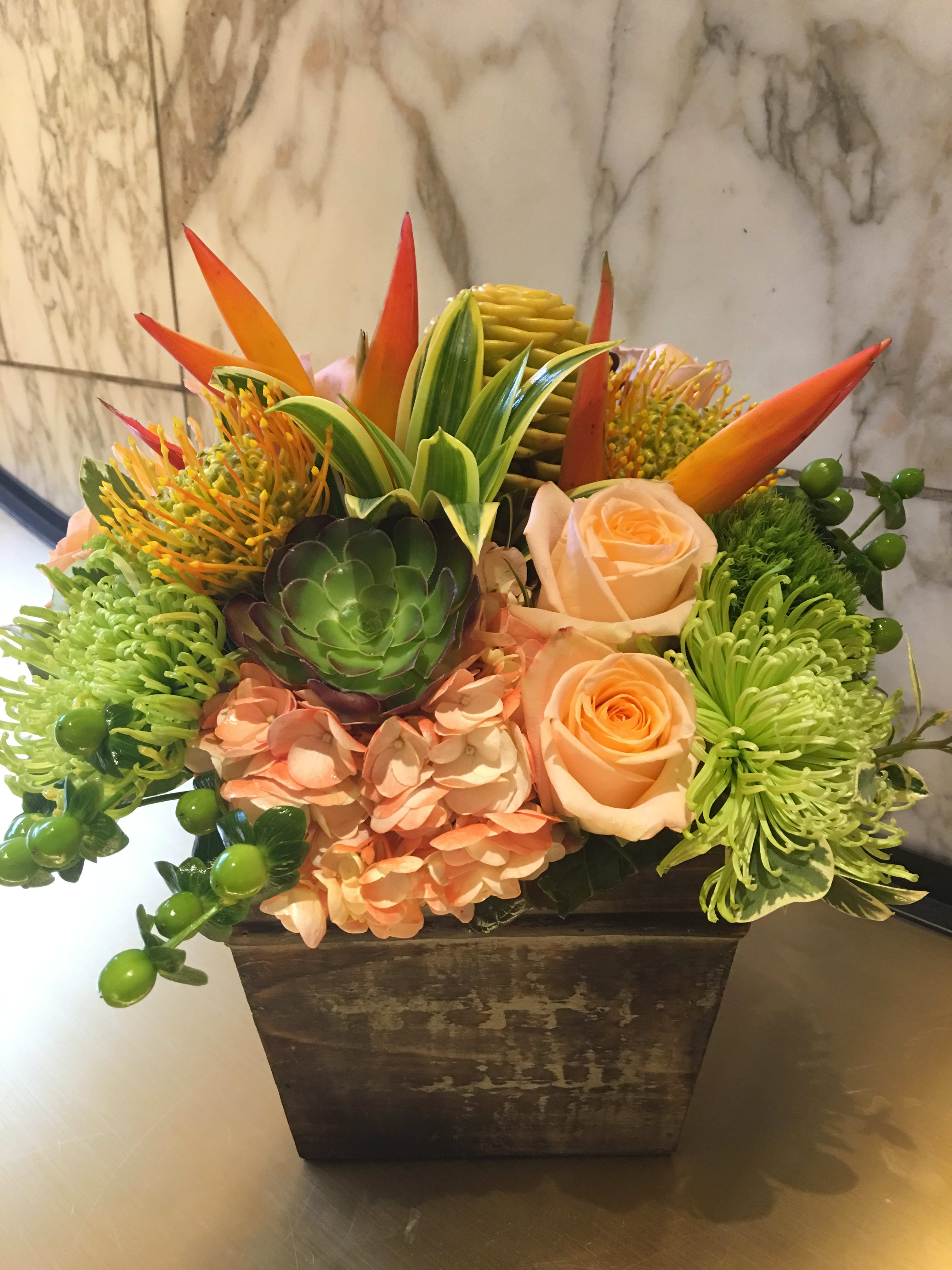 Tropical floral arrangement in a square planter with roses and succulents
