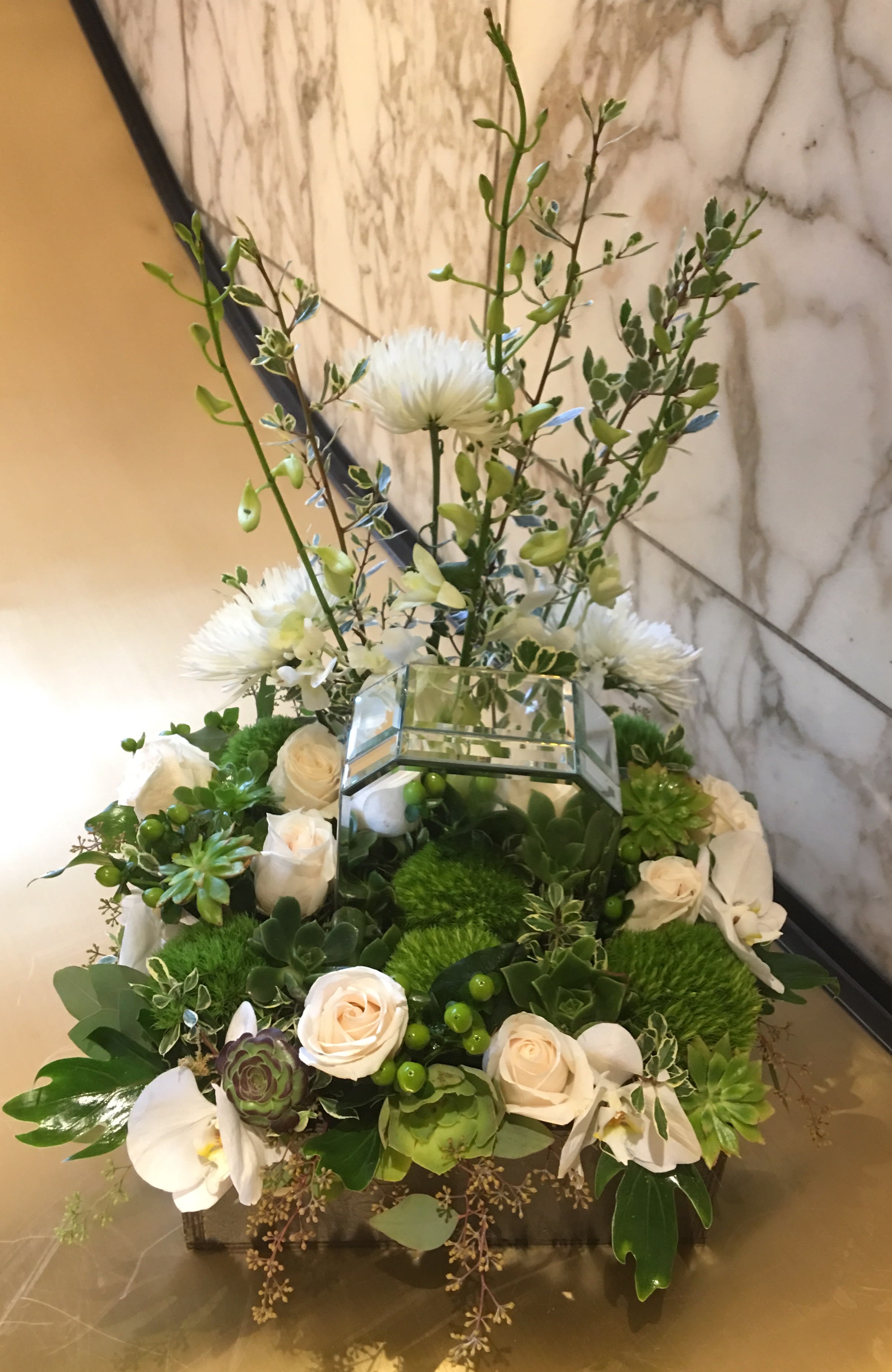 White roses and orchids arranged with succulents in a mirrored box