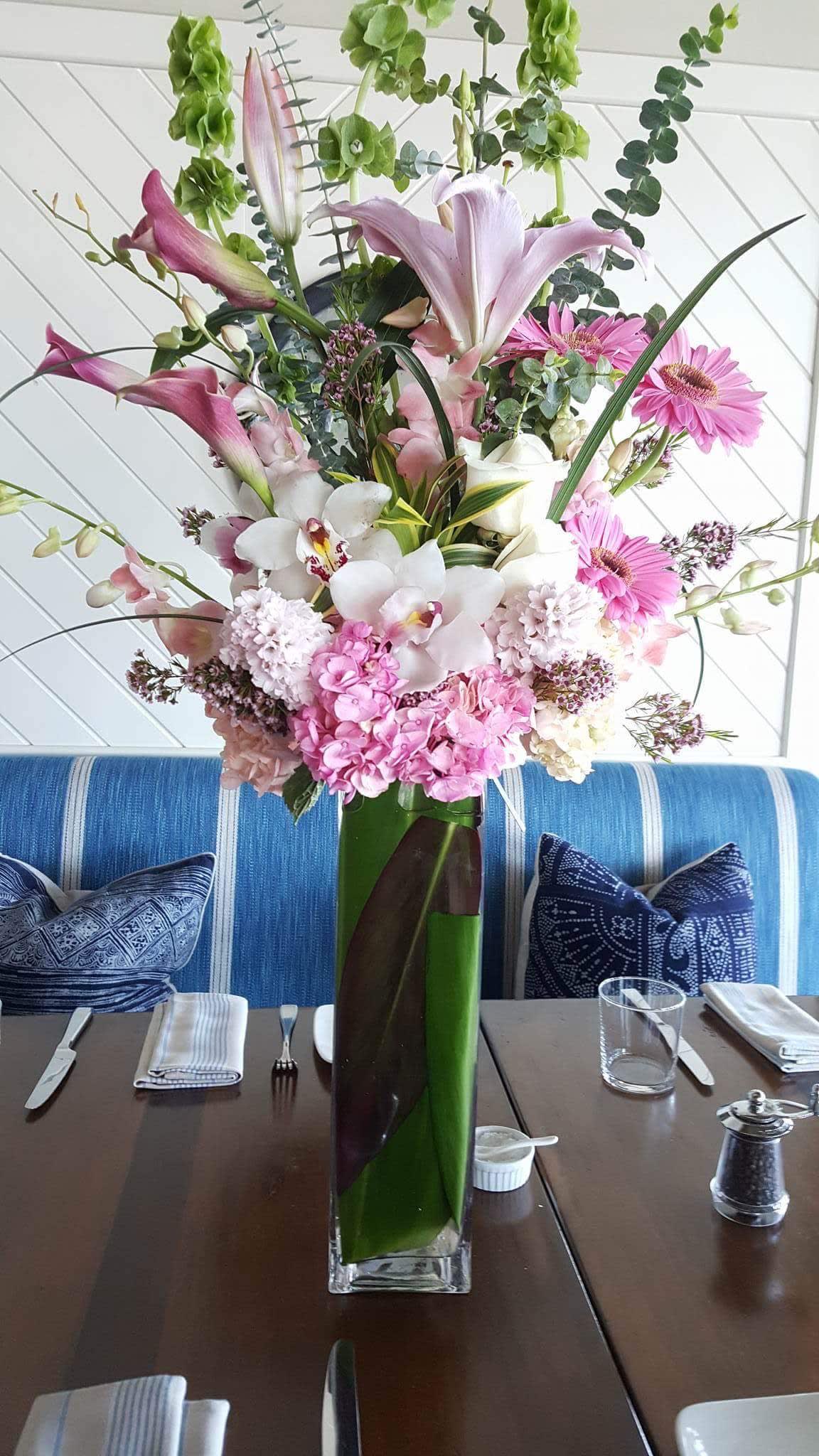 Tall pink and white floral arrangement in a glass vase on a dining table