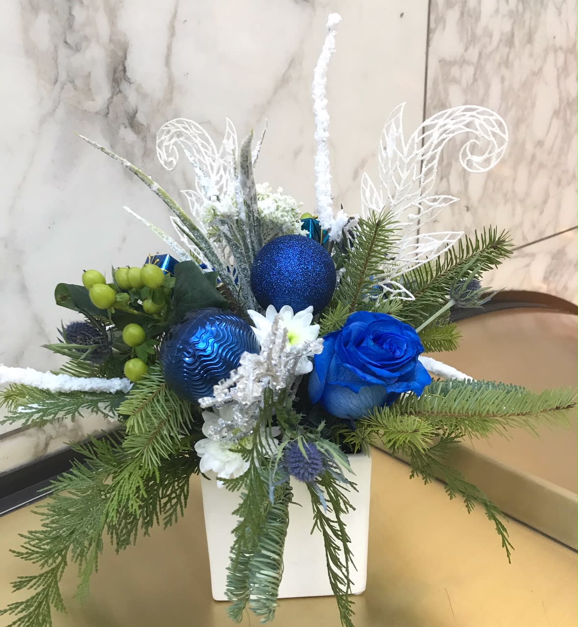 Blue rose arrangement with pine branches and ornaments in a white vase