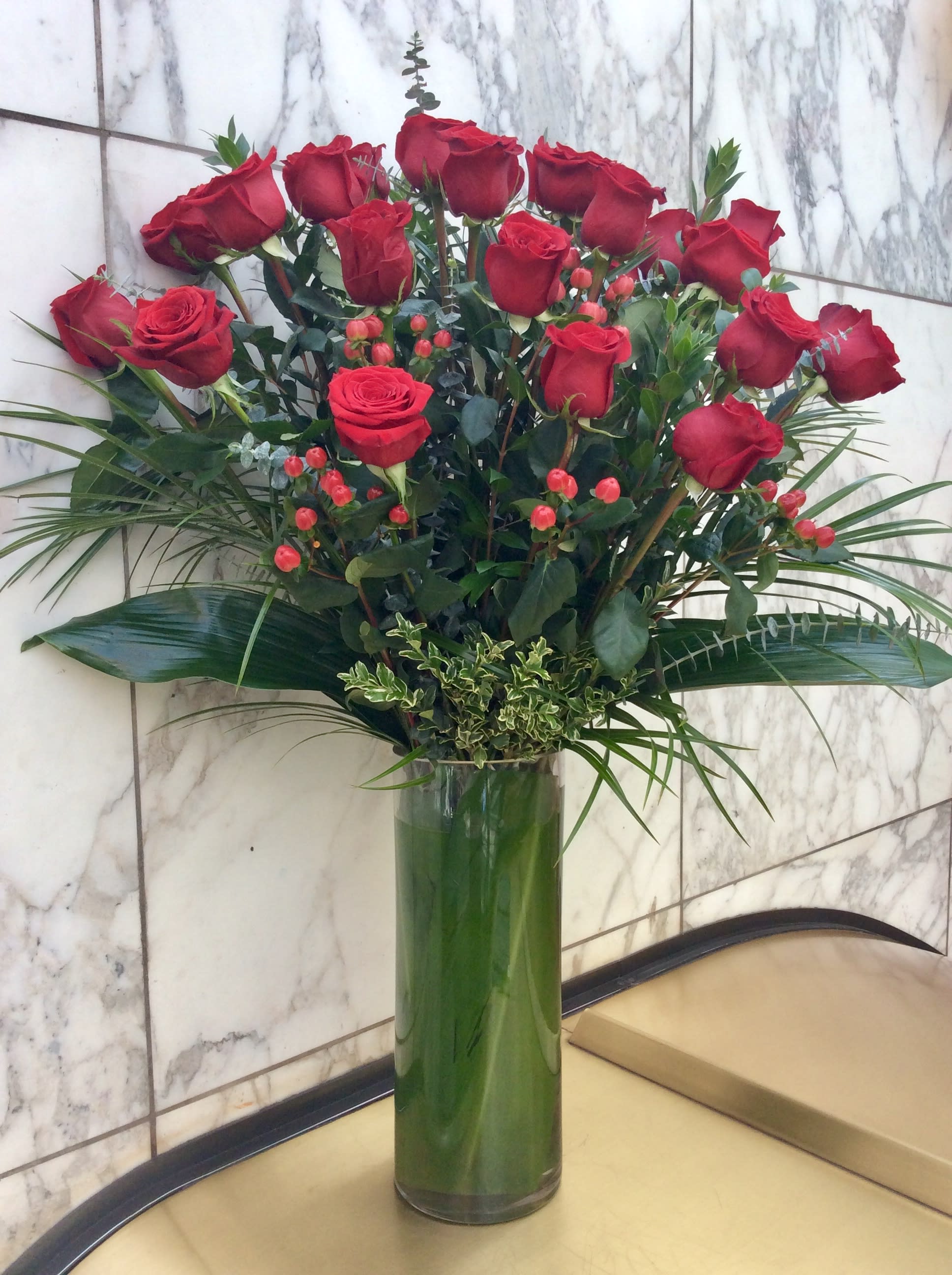 Tall vase arrangement of red roses with greenery
