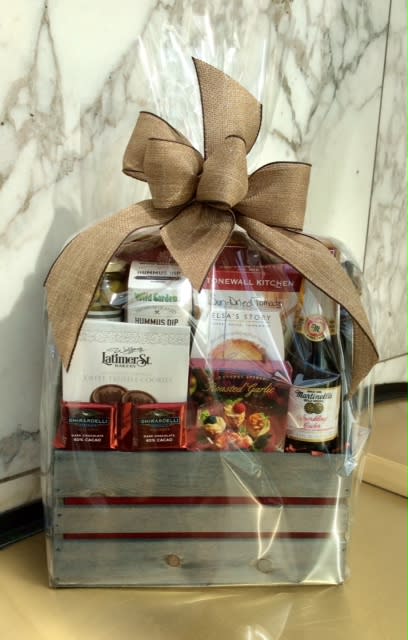 Gift basket with snacks, chocolates, and a bottle, wrapped in clear plastic with a large bow