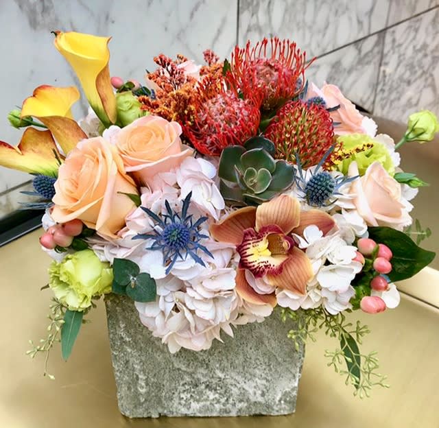 Mixed floral arrangement with roses, calla lilies, orchids, and succulents in a stone vase.