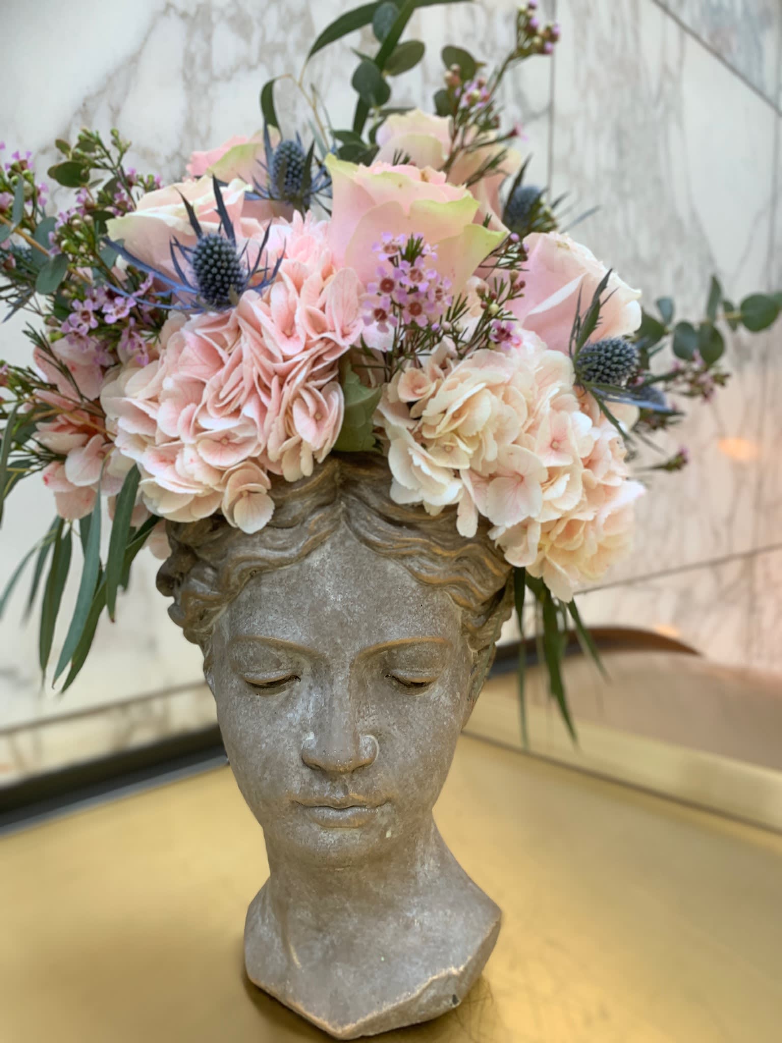 Floral arrangement in a stone bust vase with pale pink and cream blooms