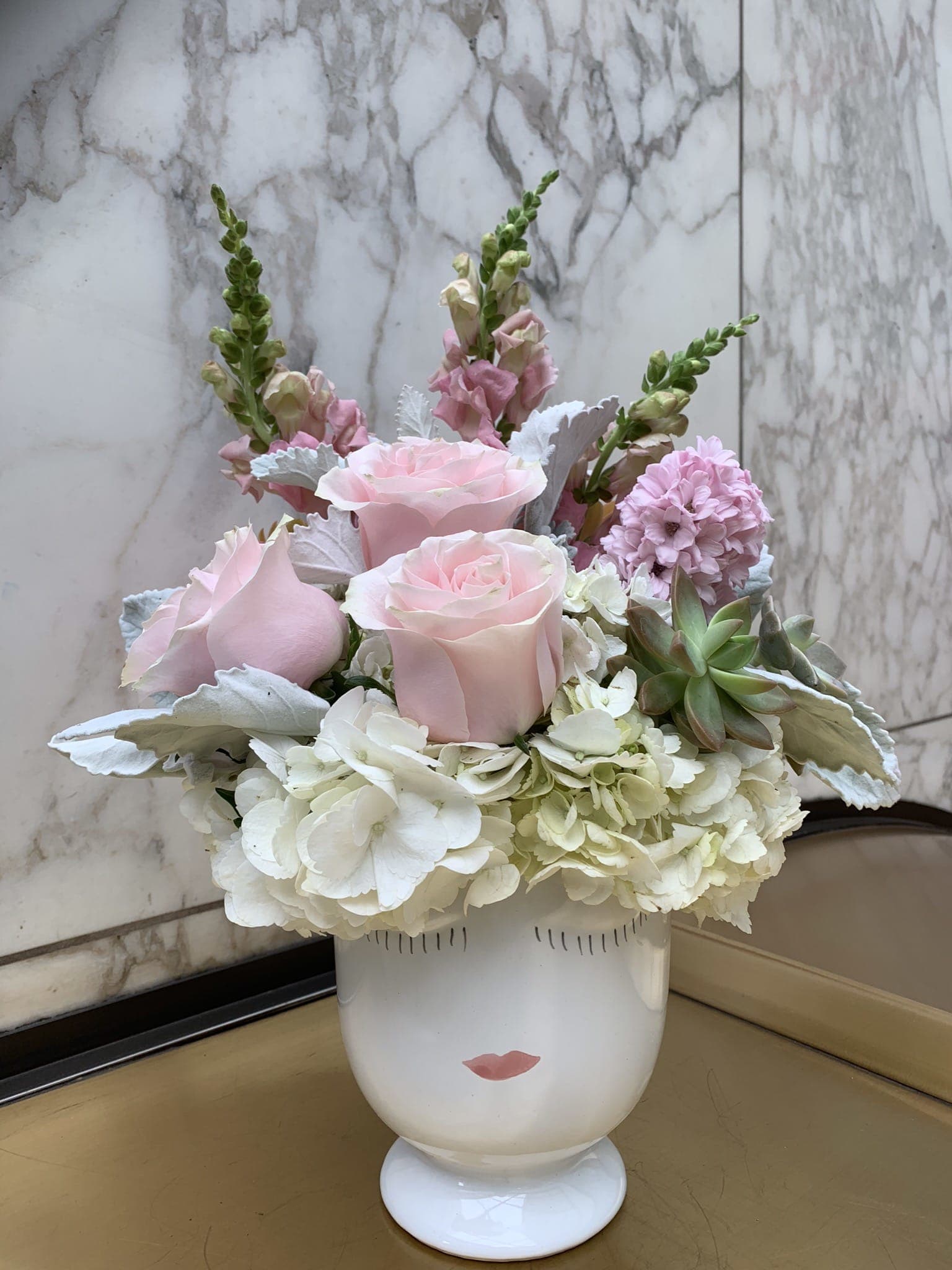 Pink roses and white hydrangeas arranged in a white vase with a face design.