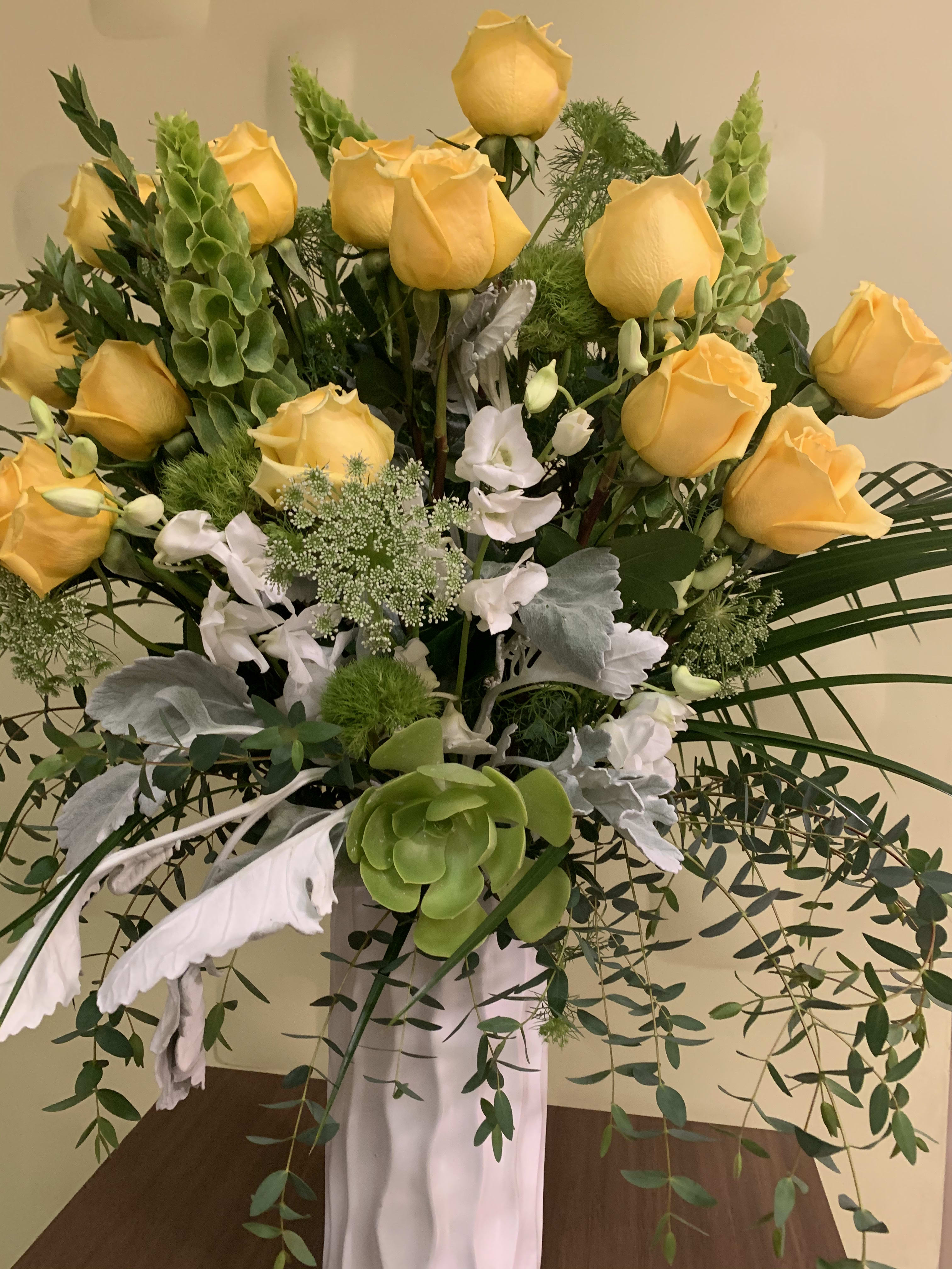 Yellow roses and white flowers in a tall arrangement with cascading greenery