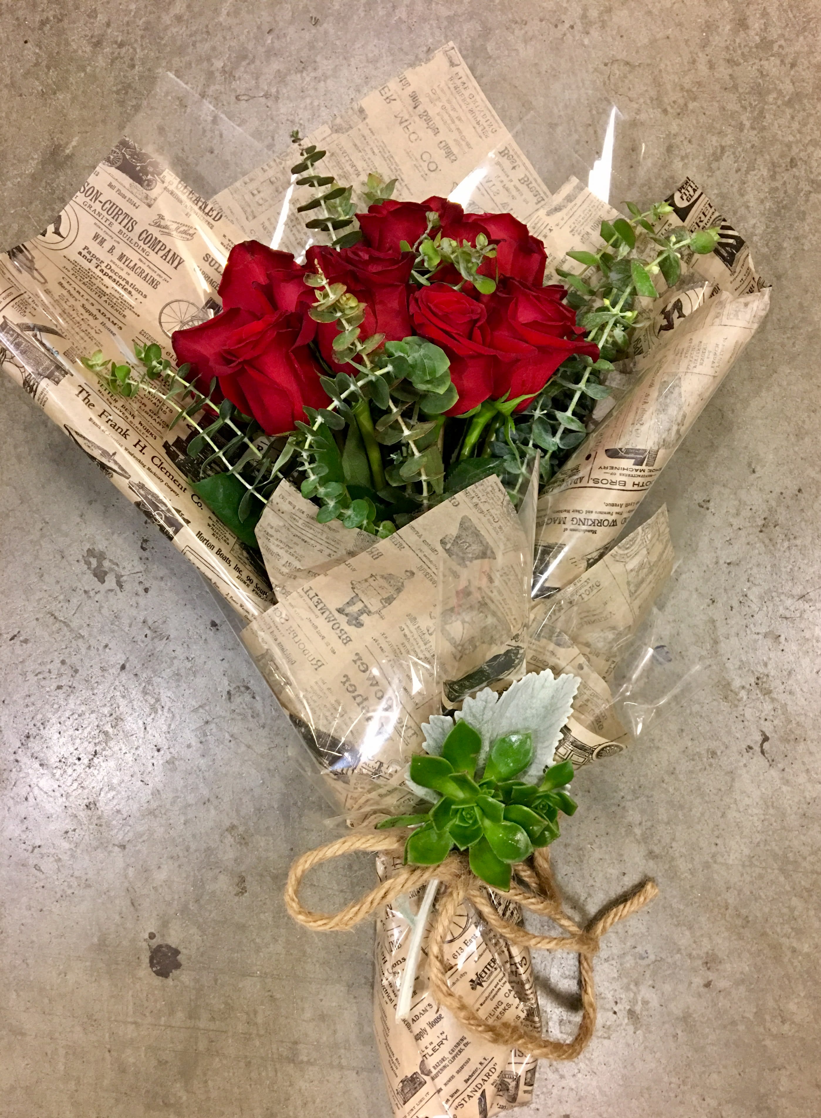Bouquet of red roses wrapped in newspaper-style paper with eucalyptus and a succulent accent