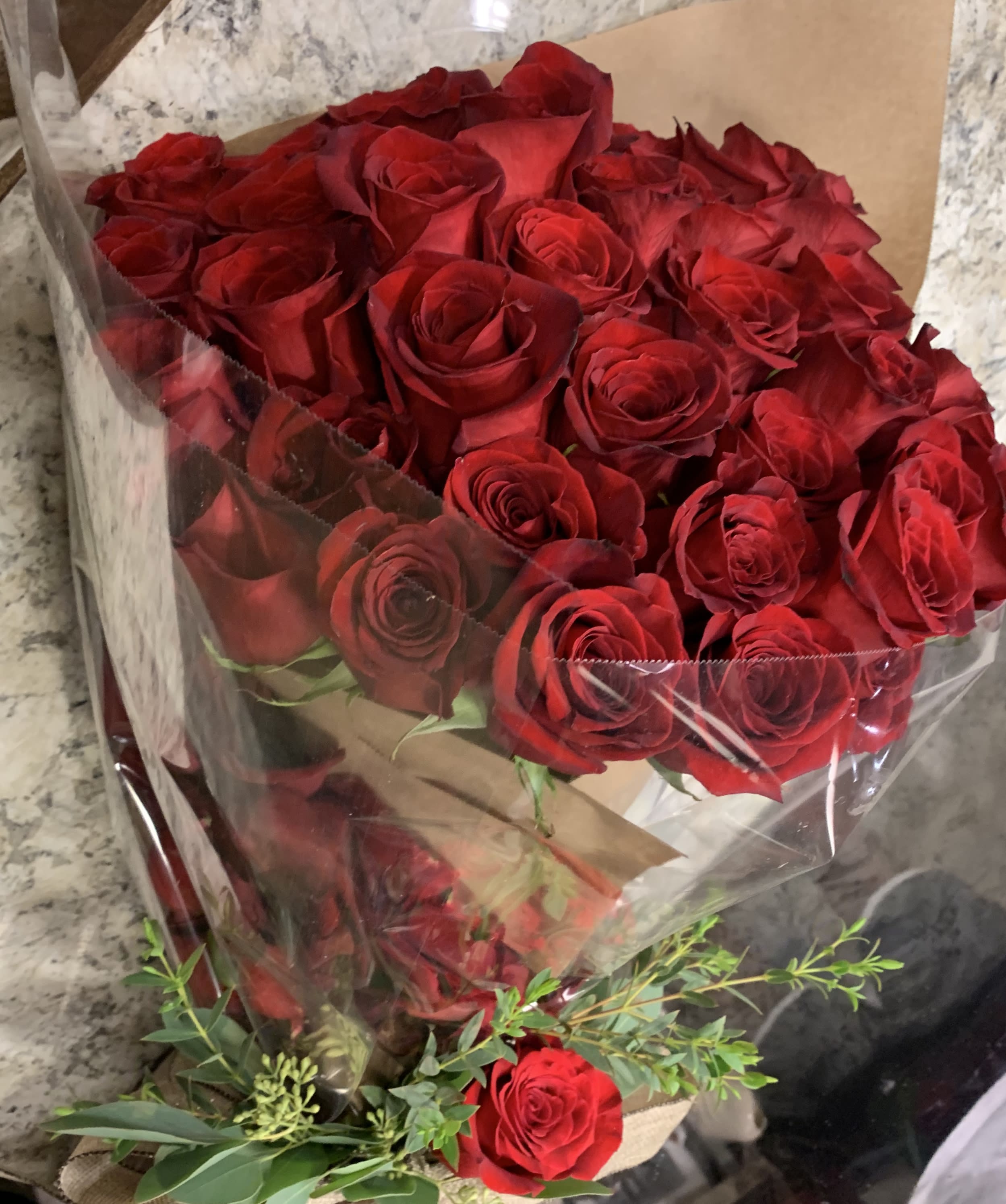 Bouquet of red roses wrapped in clear plastic with greenery