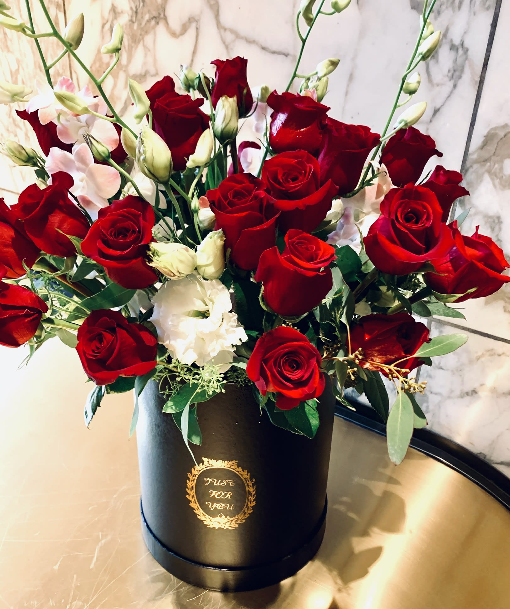 Red roses and white blooms arranged in a black hatbox