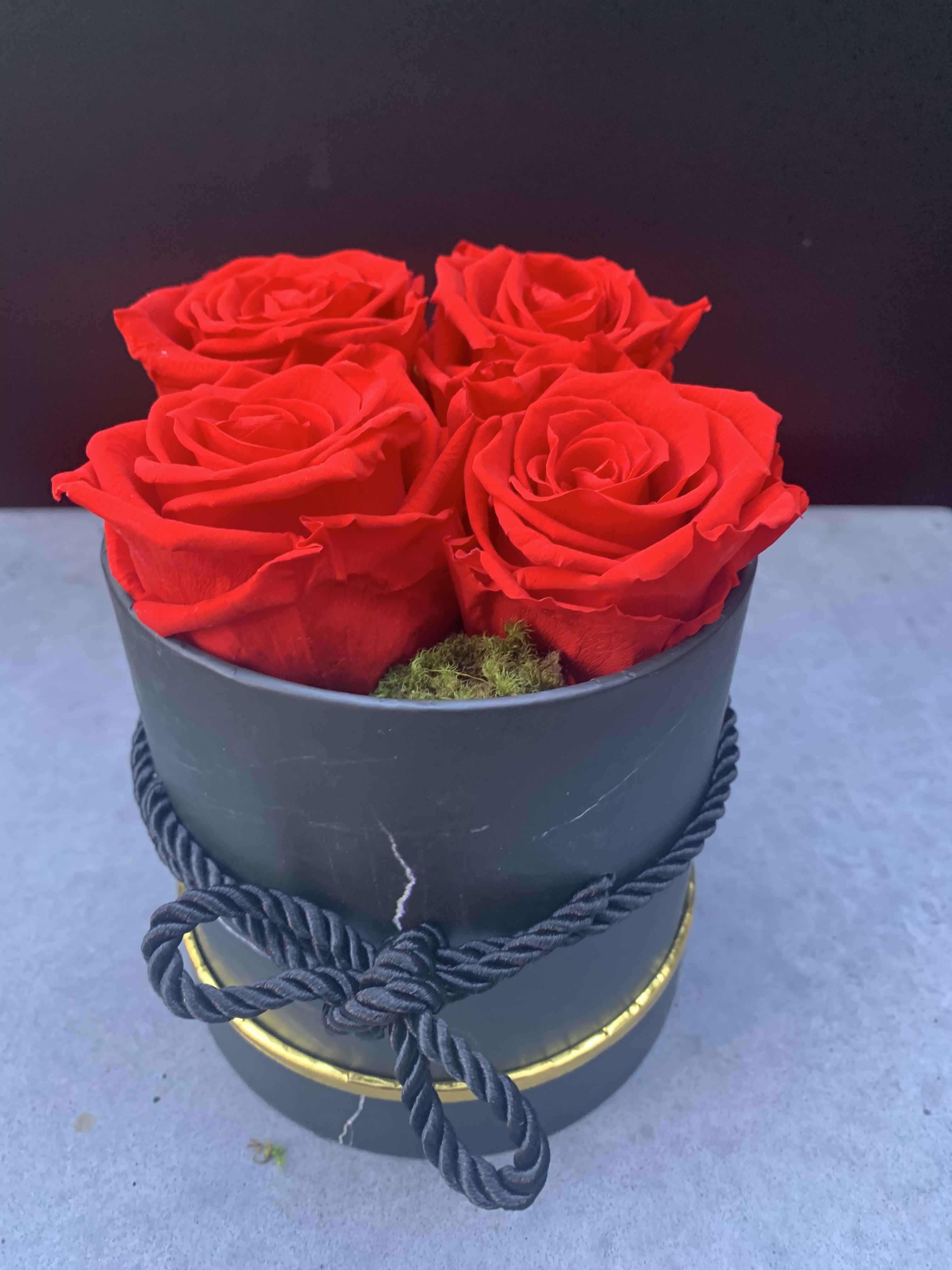 Four red roses in a black hatbox with a rope tie