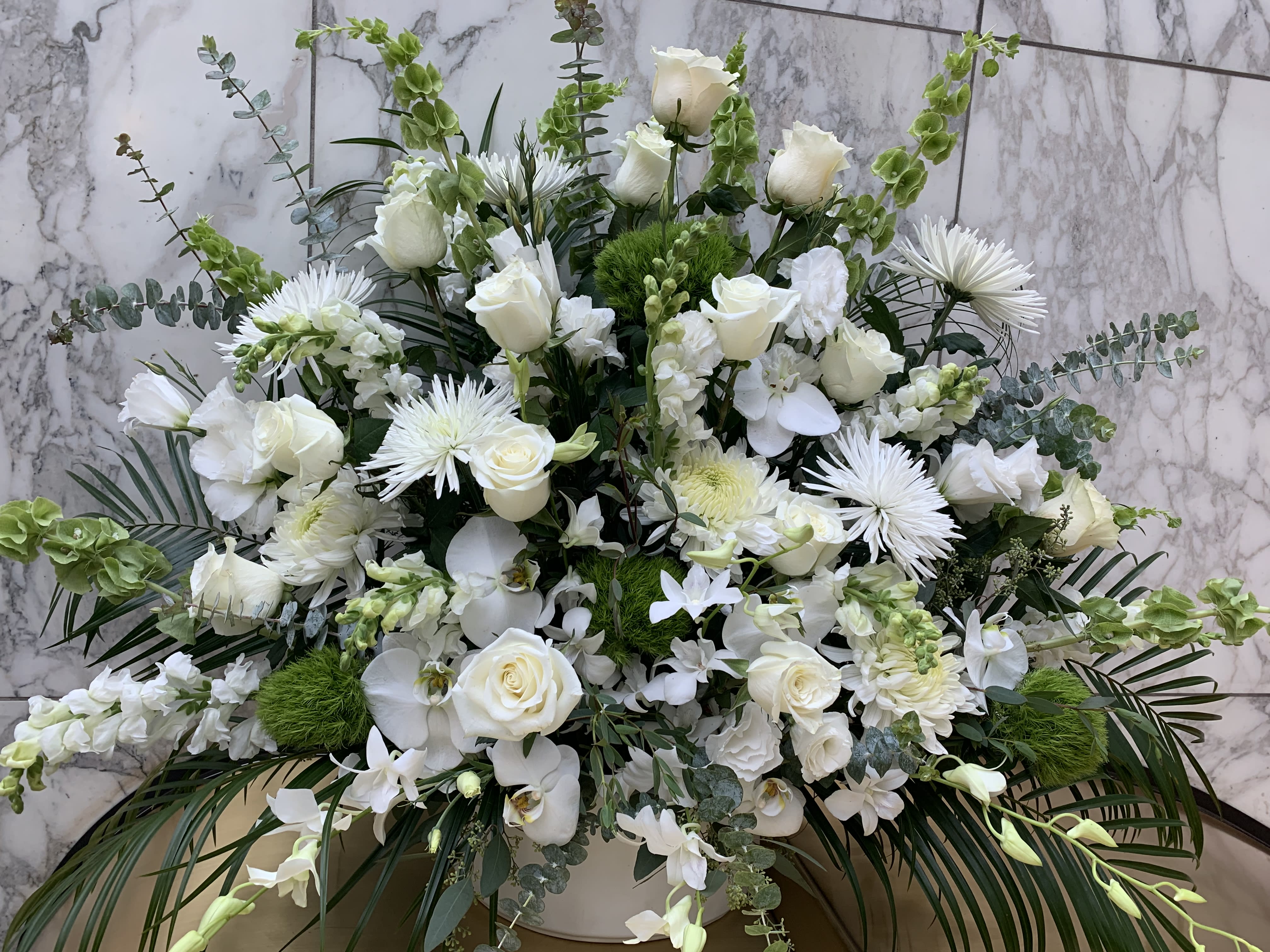 Large white floral arrangement with roses and orchids in a white container