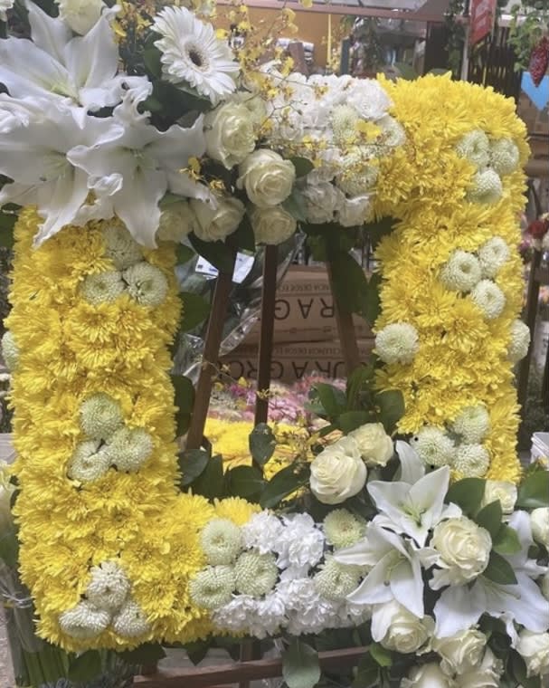 Yellow floral wreath with white lilies and roses on a stand