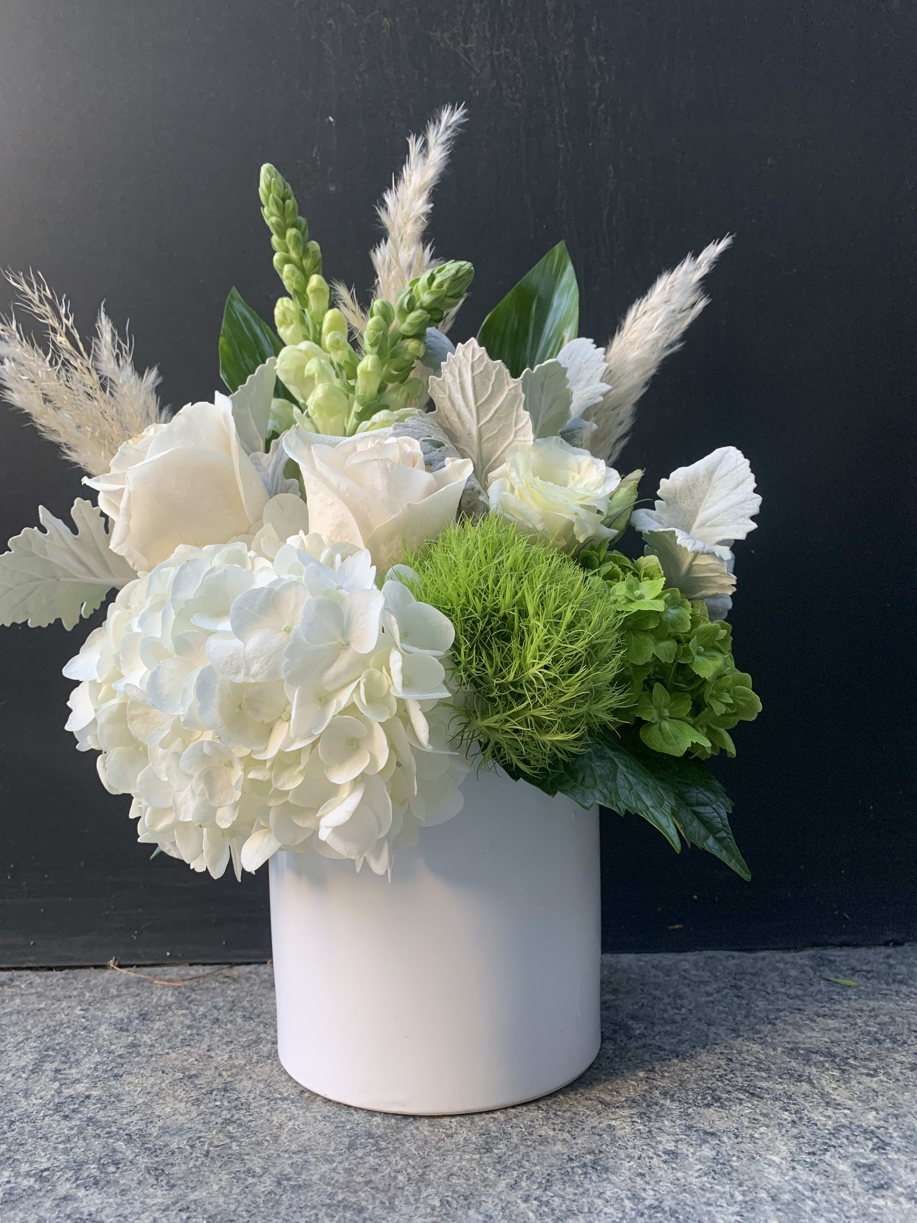 White floral arrangement in a pale cylindrical vase with green accents