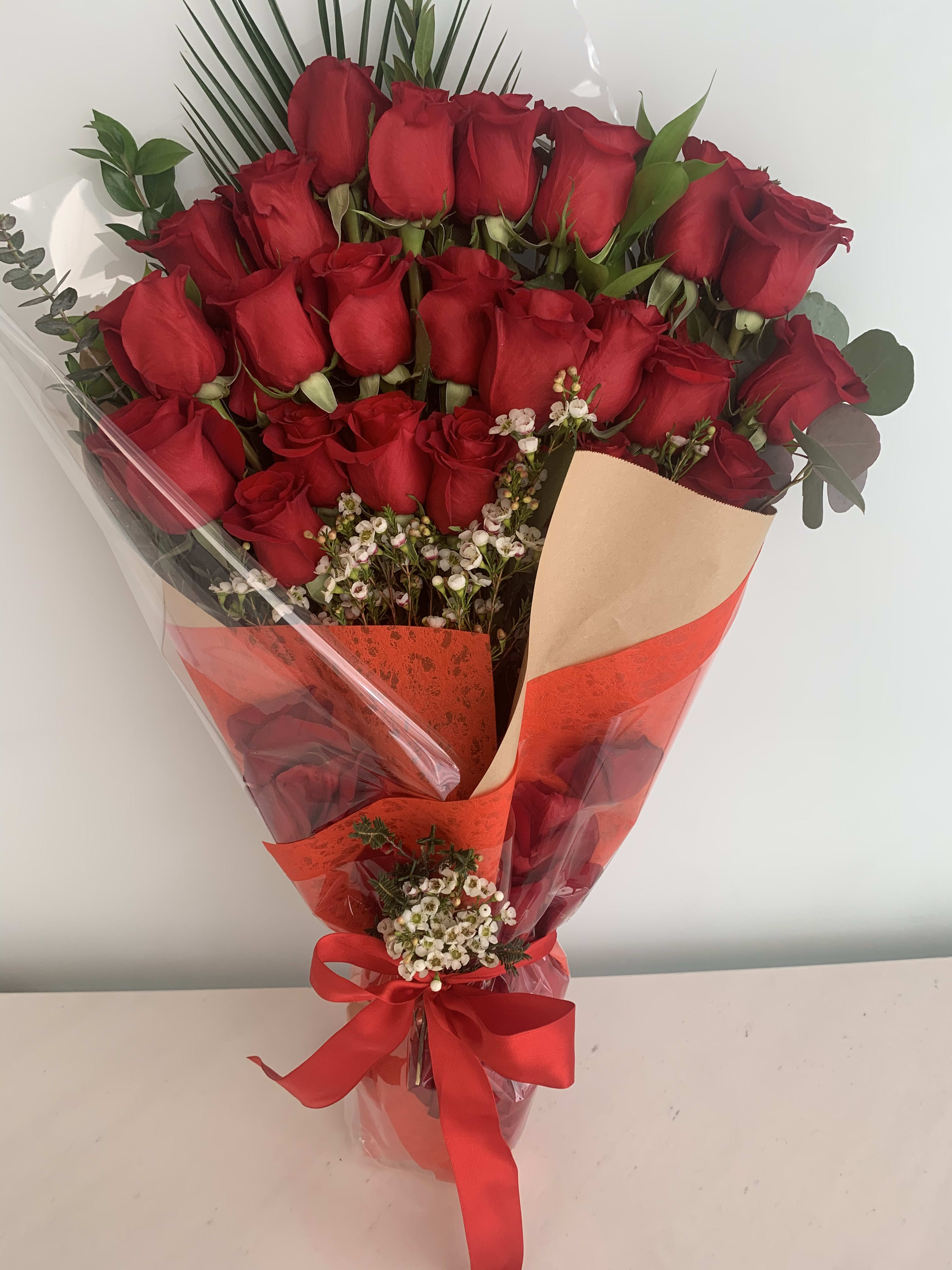 Bouquet of red roses wrapped in red and clear paper with a ribbon