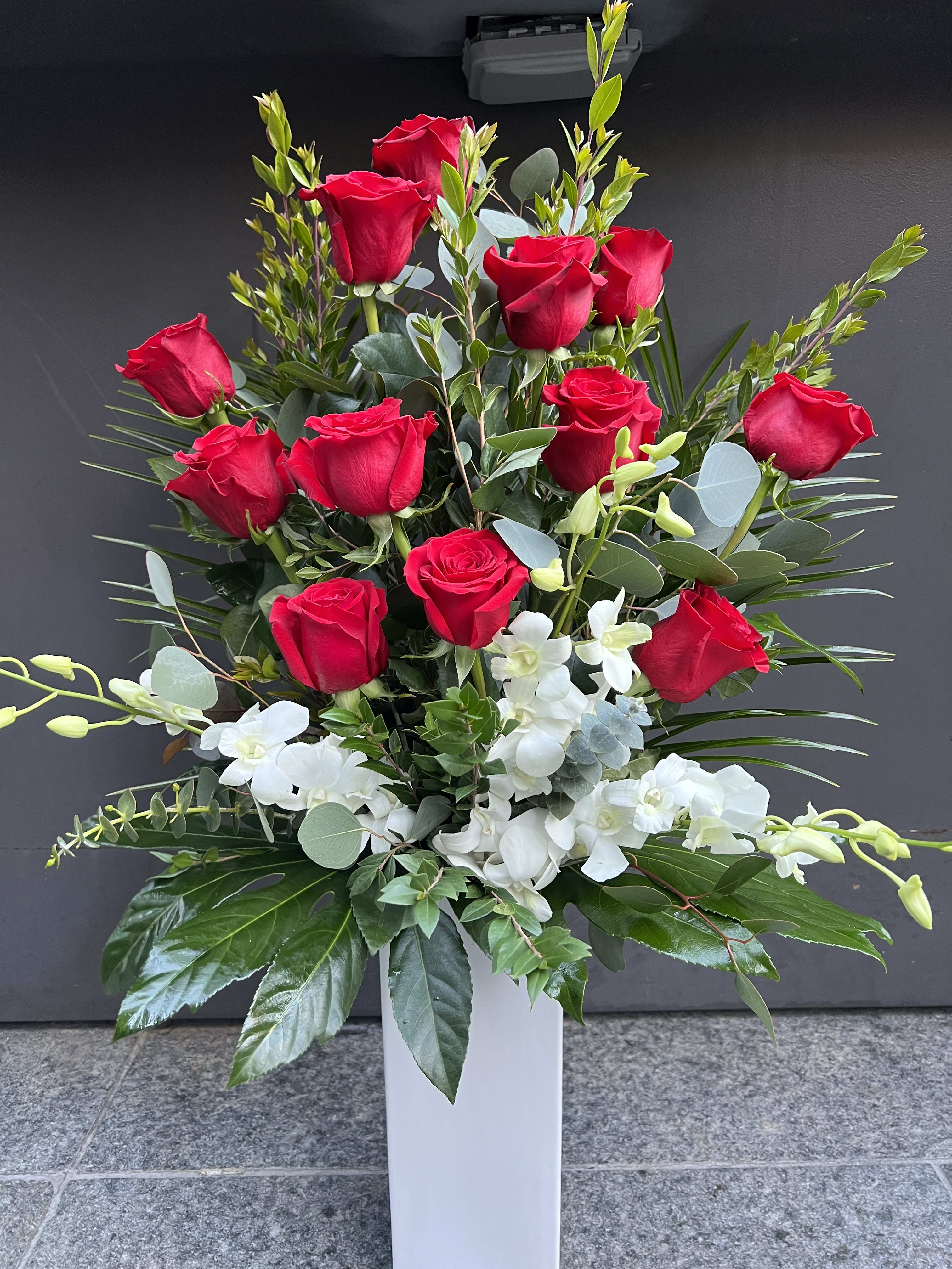 Tall arrangement of red roses and white orchids in a white vase