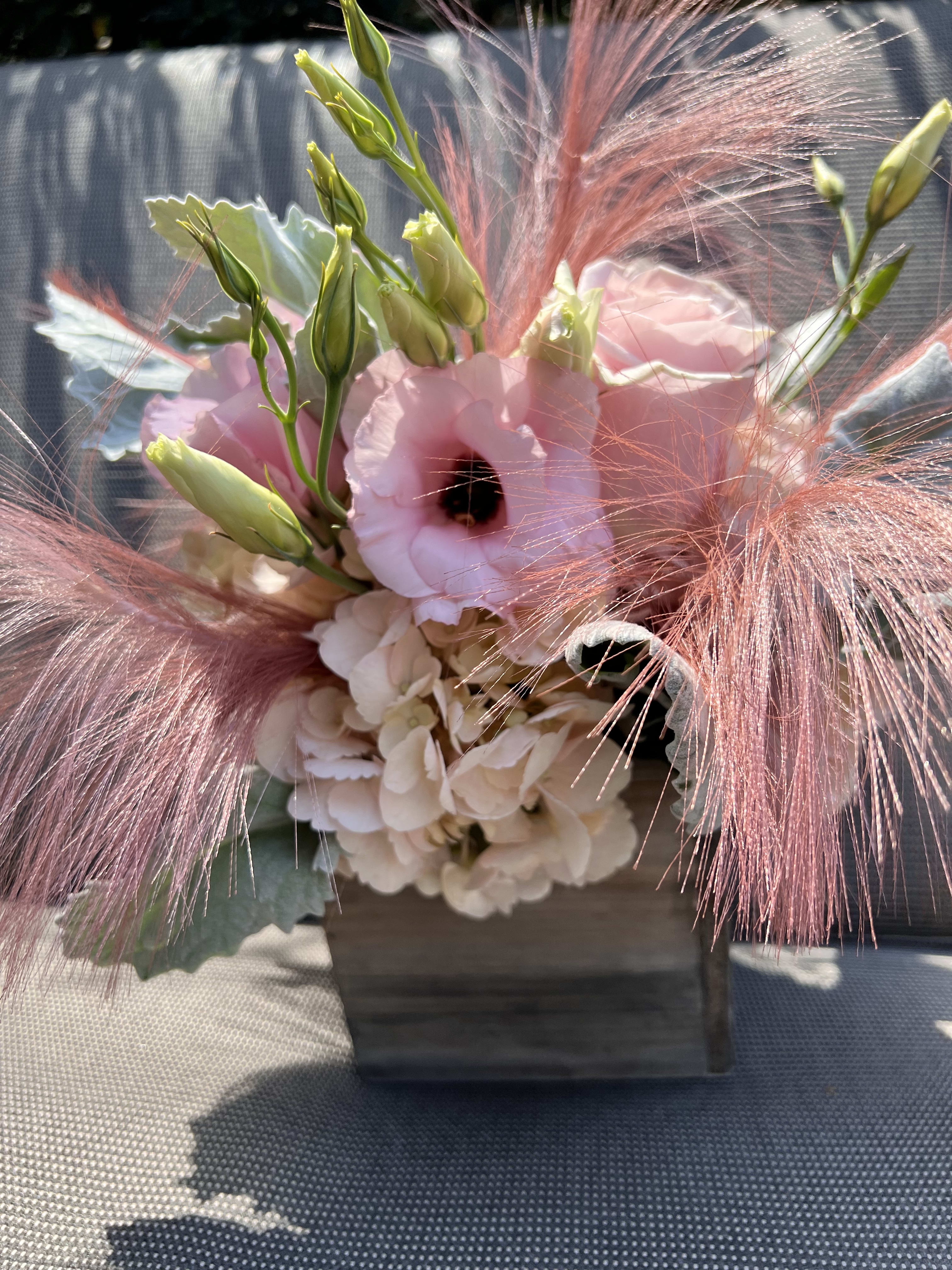 Pink and white floral arrangement with feathery pink accents in a wooden container