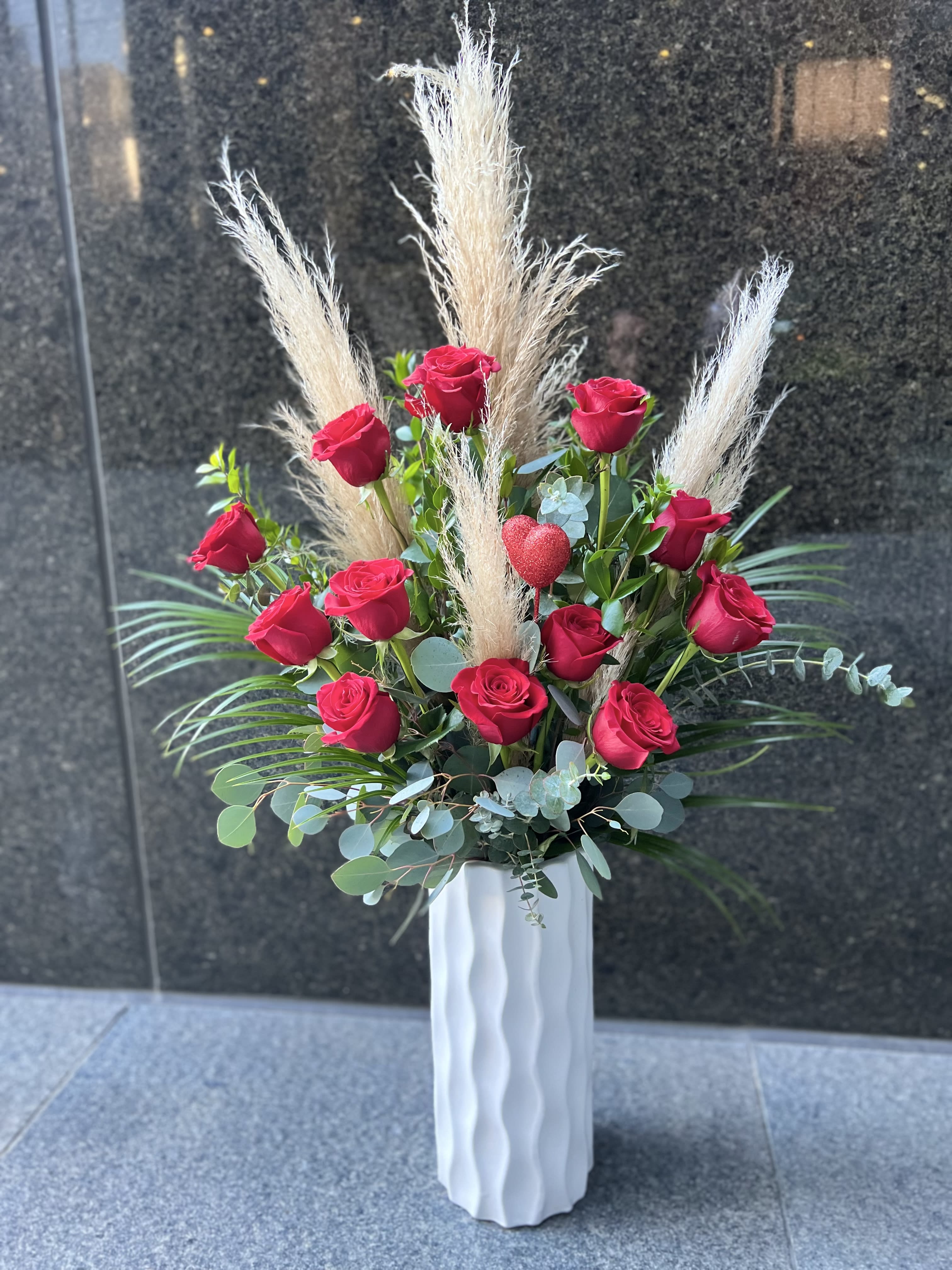 Tall arrangement of red roses with pampas grass in a white vase