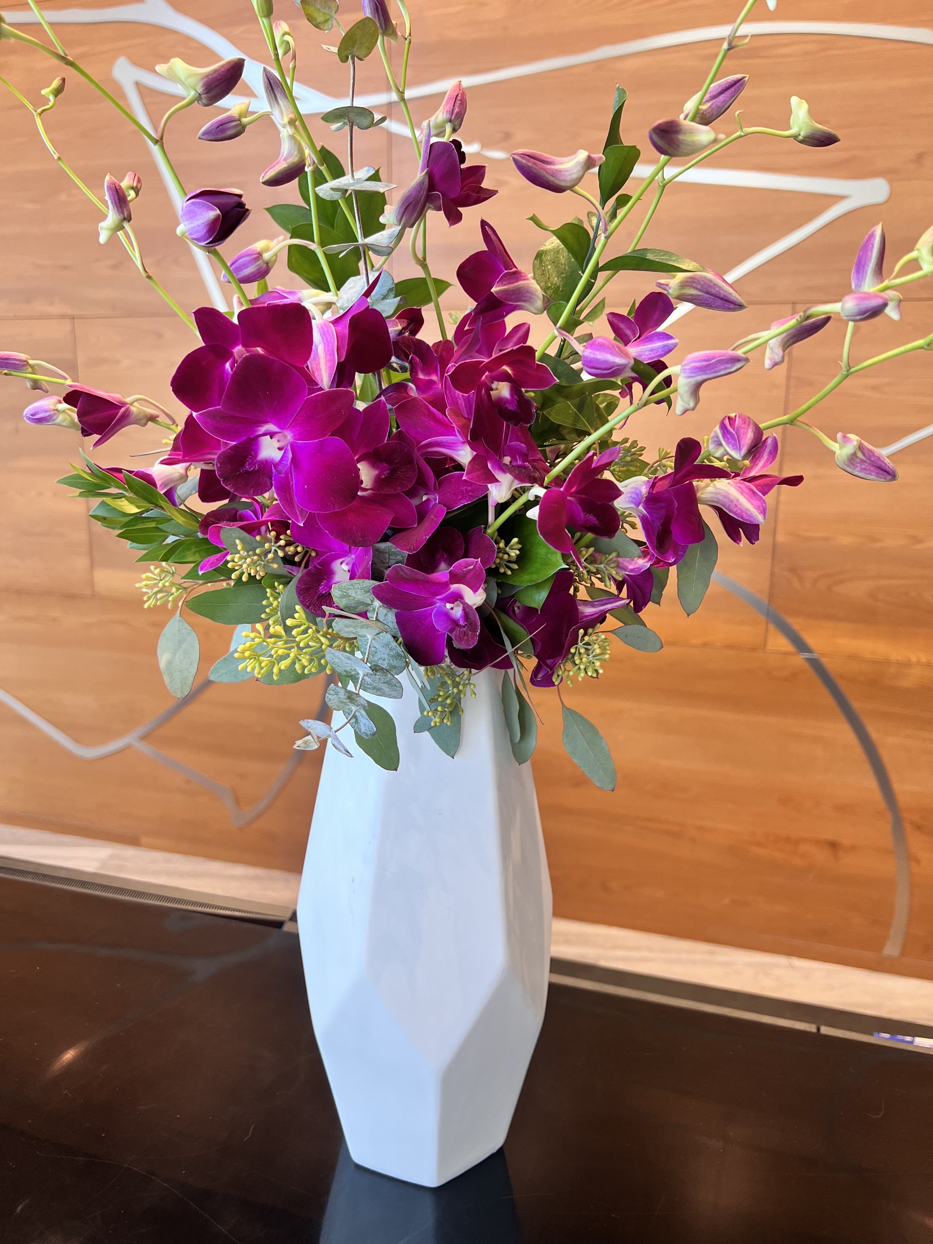Purple orchid arrangement in a tall white vase
