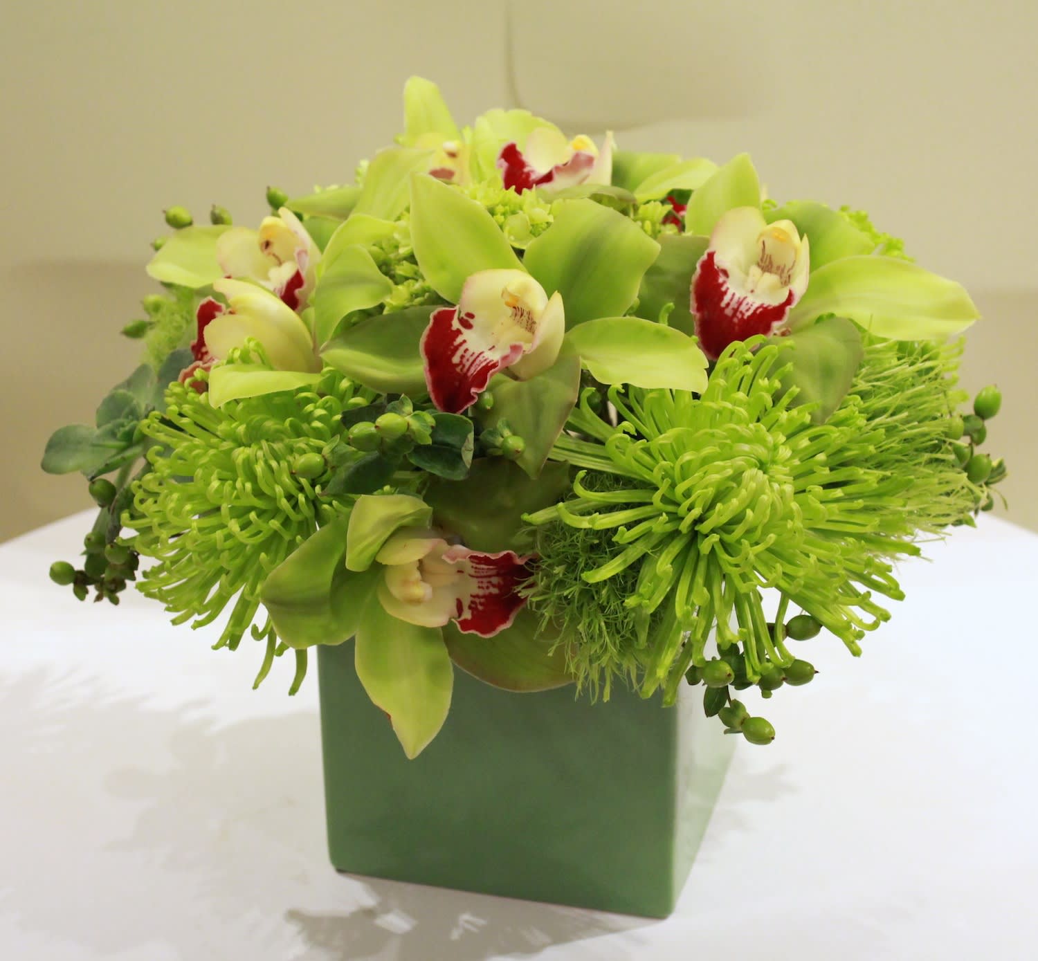 Green floral arrangement with orchids and chrysanthemums in a square vase
