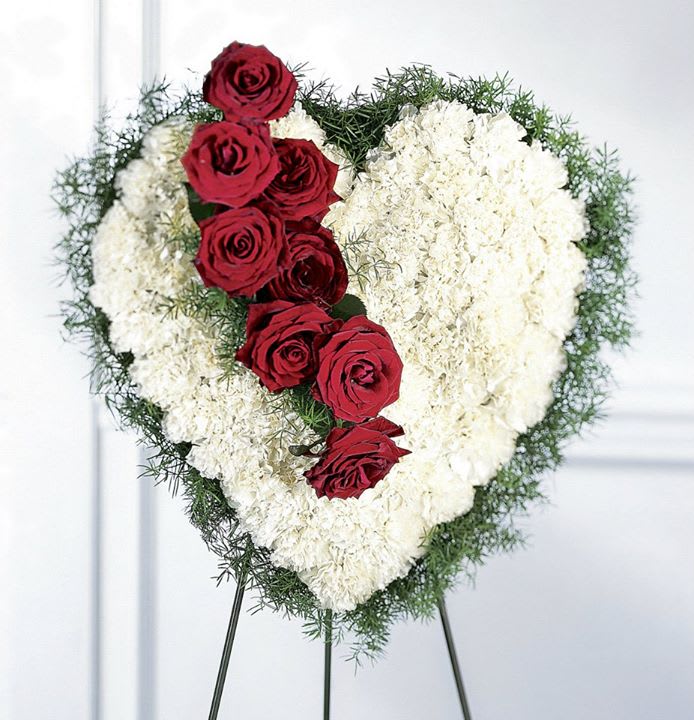 Heart-shaped floral tribute with red roses and white flowers on an easel