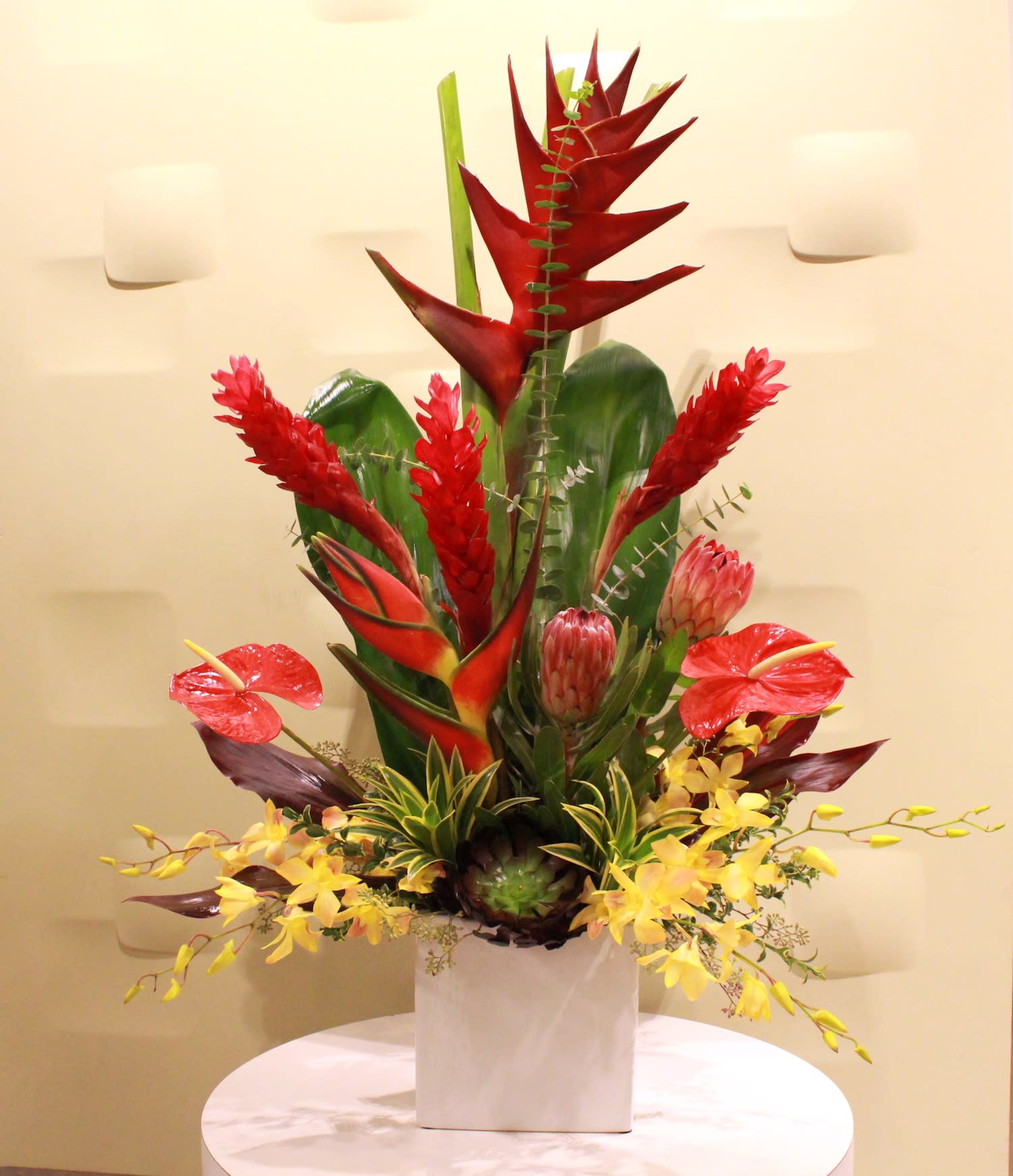 Tropical floral arrangement in a white vase with red and yellow blooms