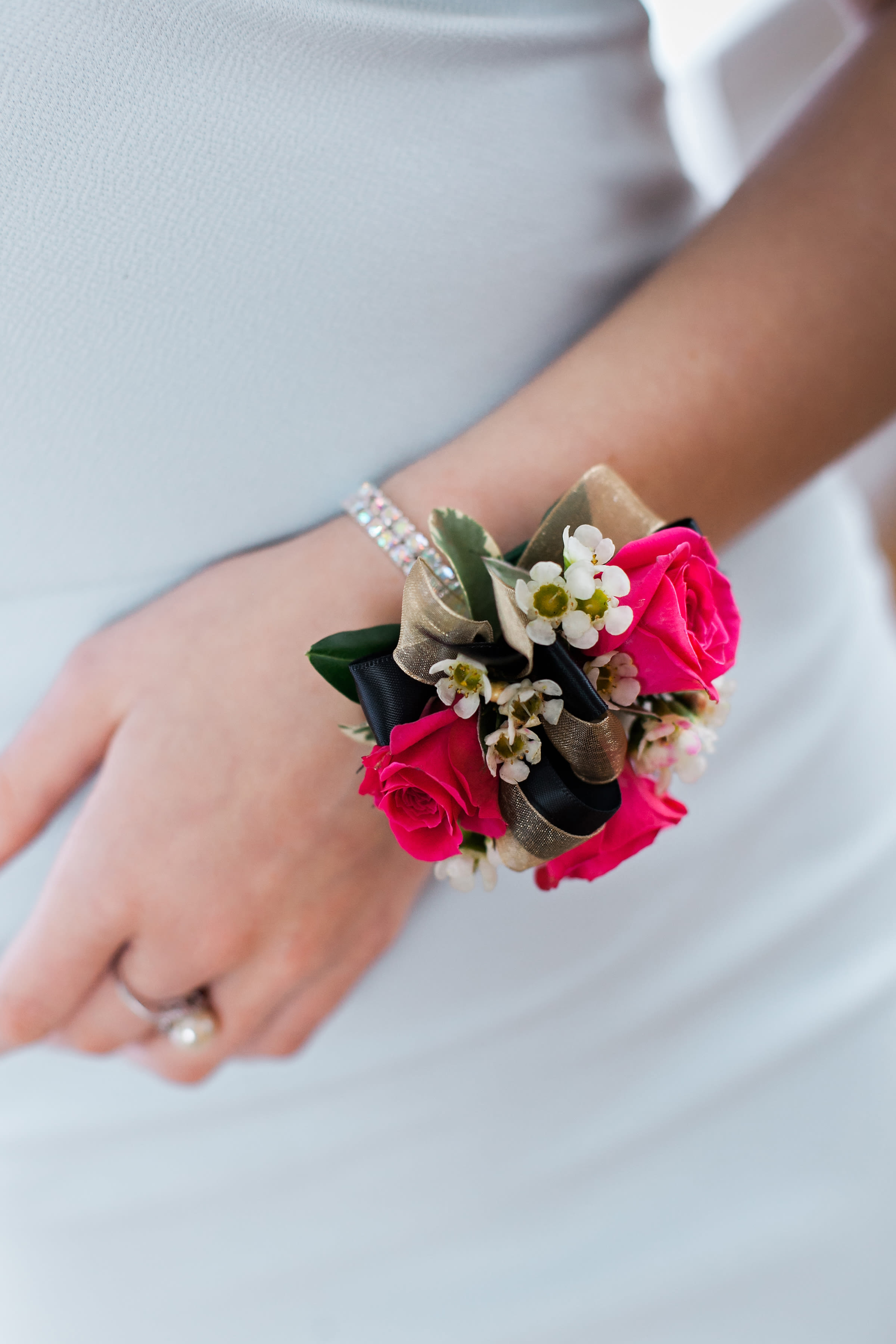 Pink rose wrist corsage with white filler flowers and ribbon on a wrist