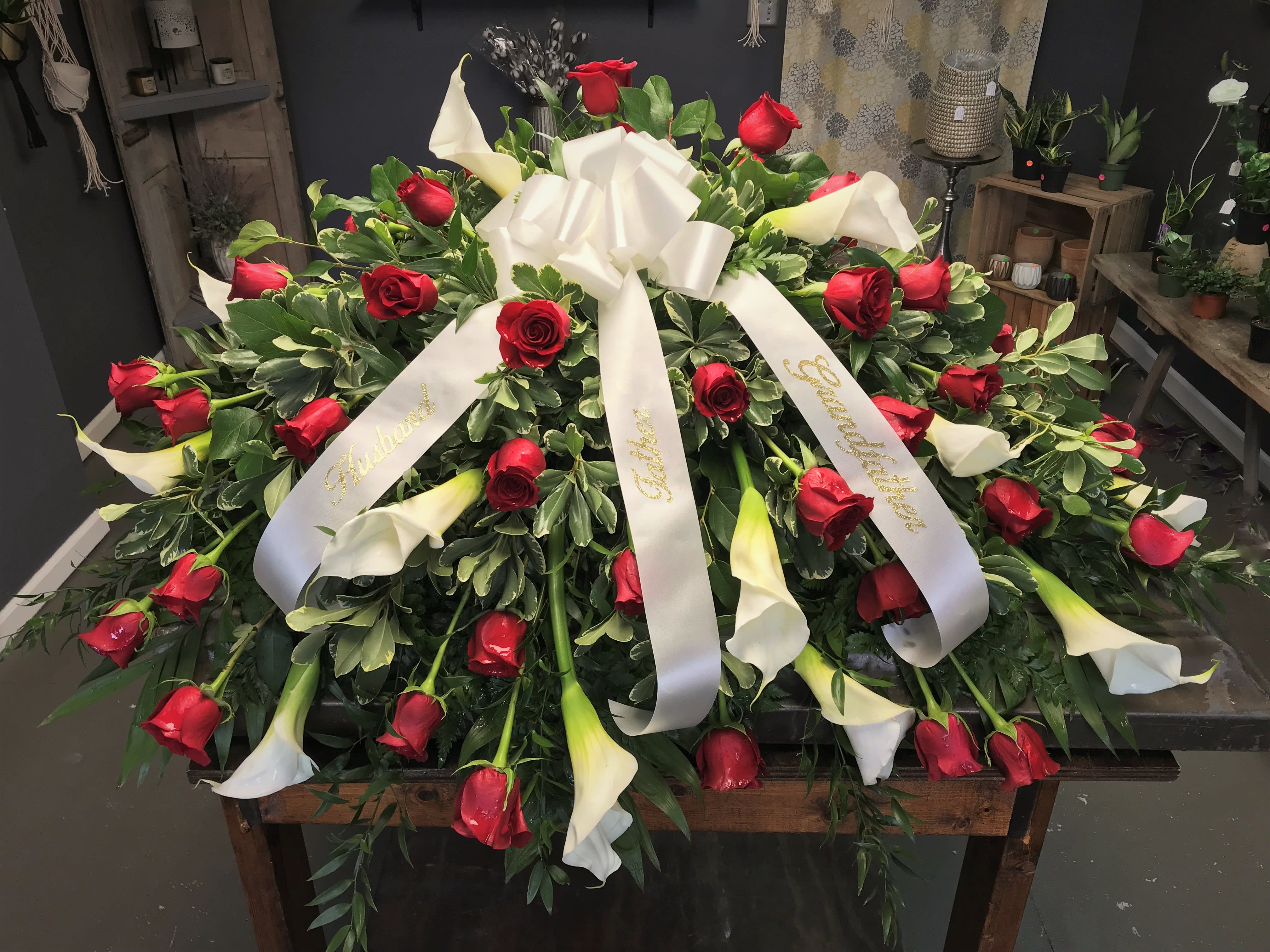 Large funeral spray of red roses and white calla lilies with white ribbons