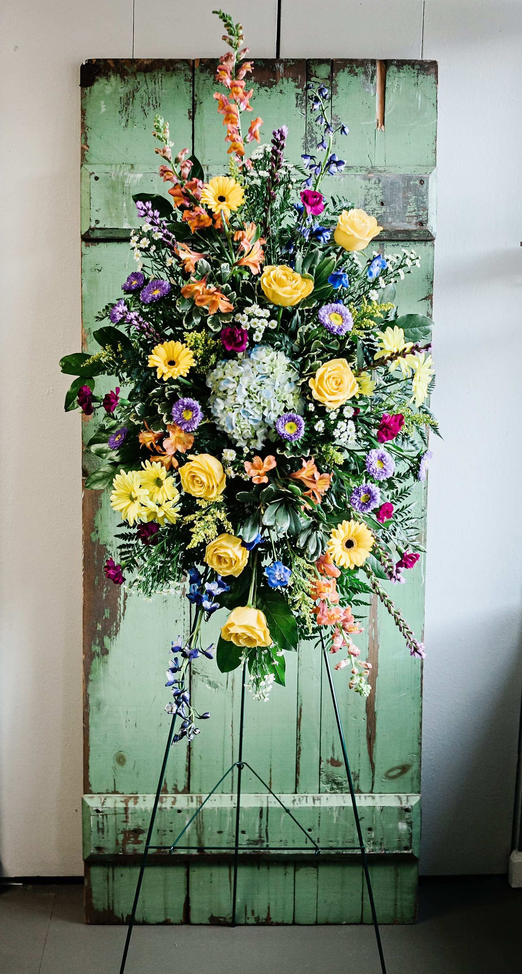 Tall mixed floral spray on a stand with yellow roses and purple blooms