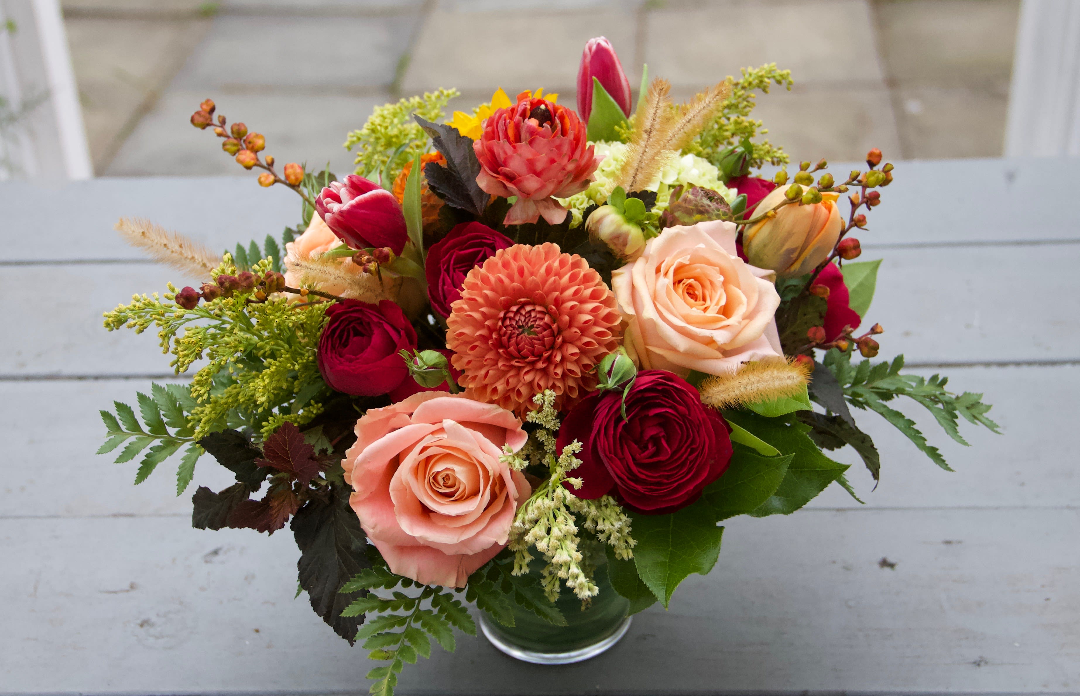 Mixed bouquet of roses, dahlias, and tulips in a glass vase