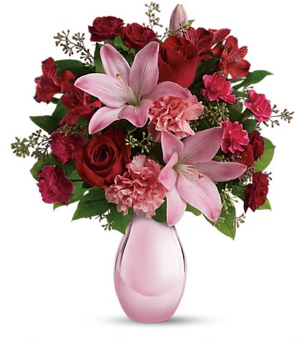 Pink lilies and red roses arranged in a pink glass vase