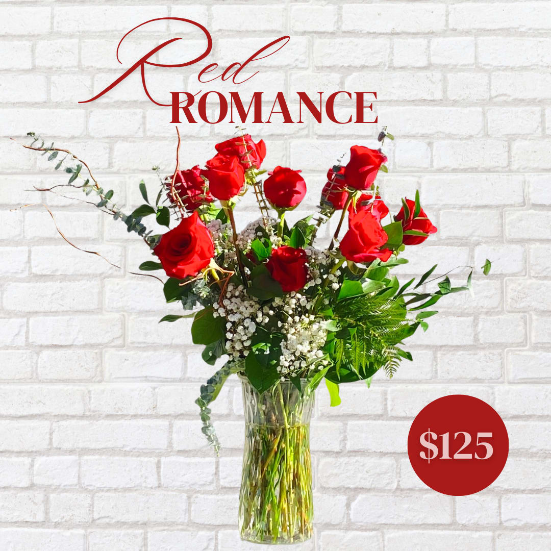 Red roses arranged in a tall glass vase with white filler flowers.