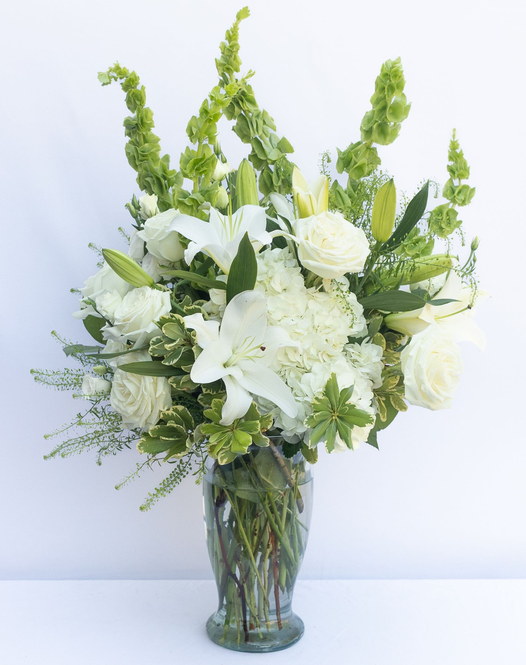 Hope Heals Luxury Bouquet  - Offering a ray of light within what can be a dark place when grieving the loss of a loved one, The Hope Heals™ Luxury Bouquet is a unique and sophisticated way to show how much you care for your recipient and the memory of the deceased. An exquisite arrangement designed by our floral experts, this gorgeous bouquet brings together ivory roses, fragrant white gilly flowers, clouds of white hydrangea and star-shaped white Asiatic Lilies. Accented with asparagus fern fronds and variegated foliage, this sympathy bouquet is presented in a keepsake faceted clear glass vase to create an exceptional look that is not only a tribute to a life well lived, but a comfort to those left behind. IMPRESSIVE bouquet is approx. 23"H x 19"W. STUNNING bouquet is approx. 25"H x 21"W.