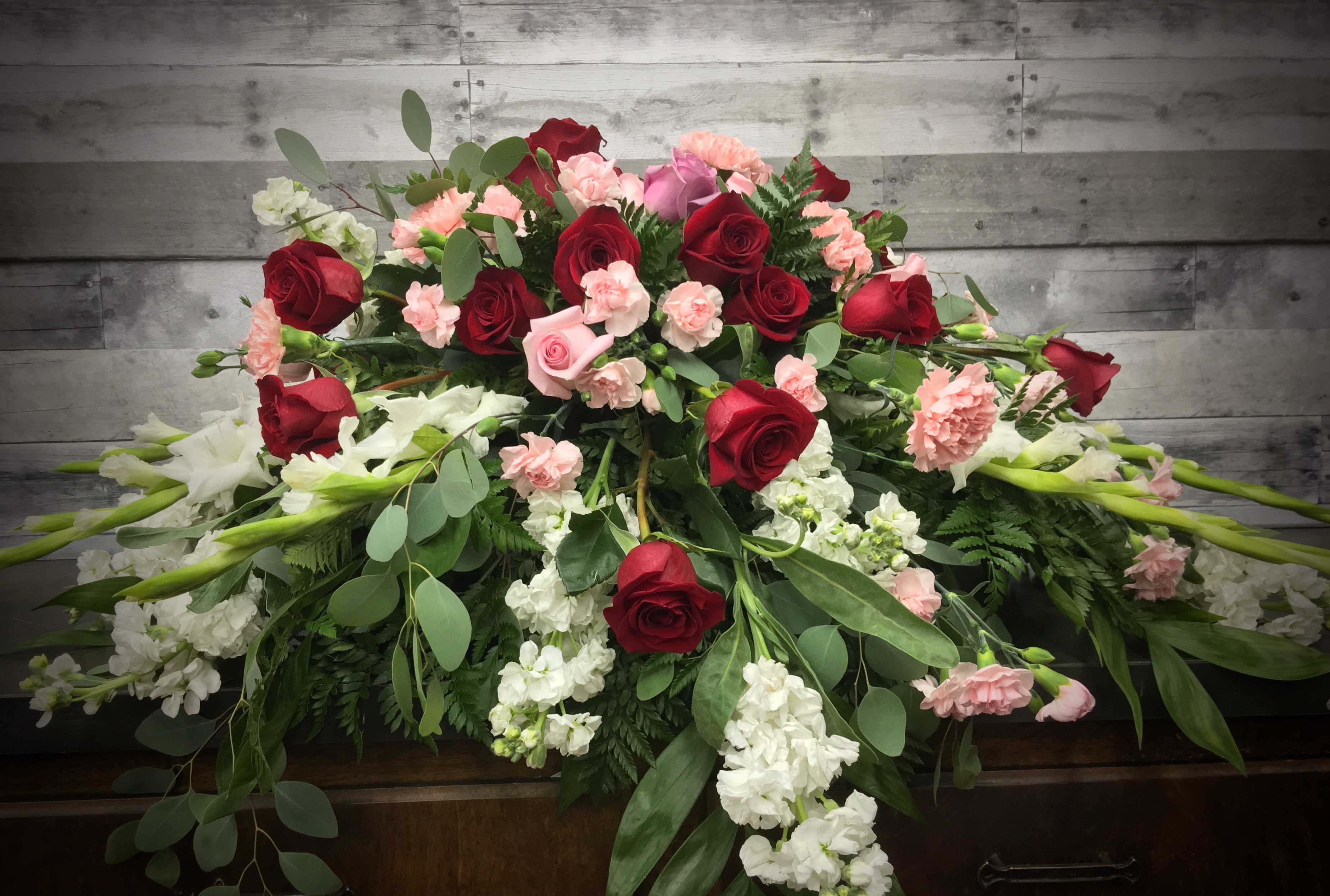 Casket spray with red and pink roses, carnations, and white flowers