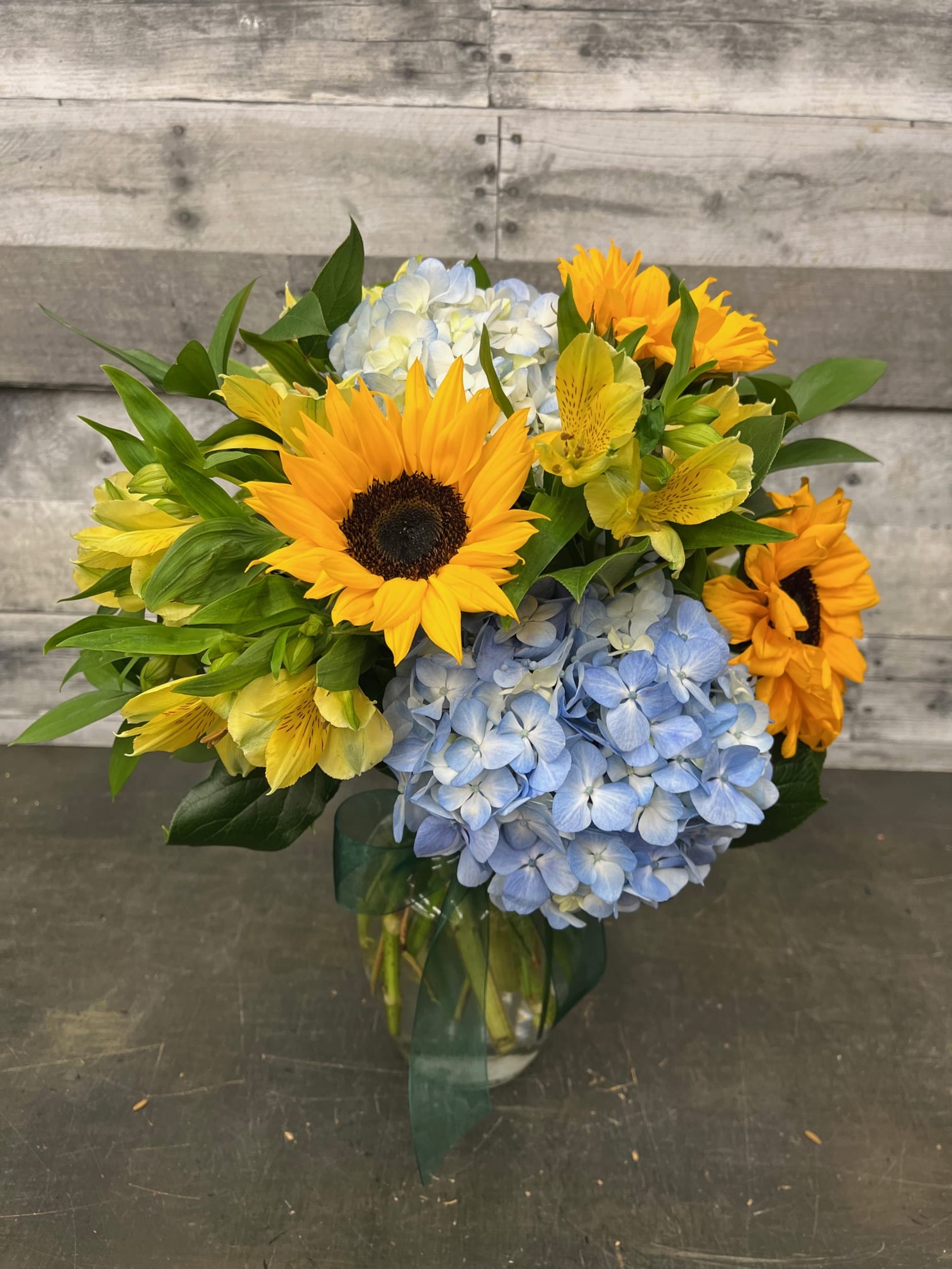 Bouquet of sunflowers, blue hydrangeas, and yellow alstroemeria in a glass vase