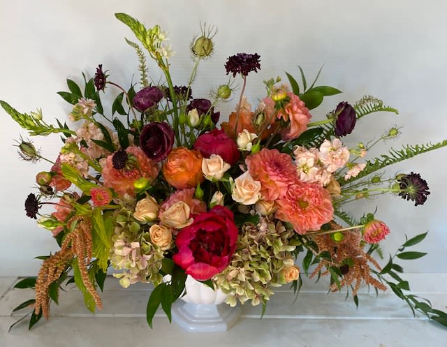 Large mixed bouquet in a white vase with pink, peach, and burgundy blooms