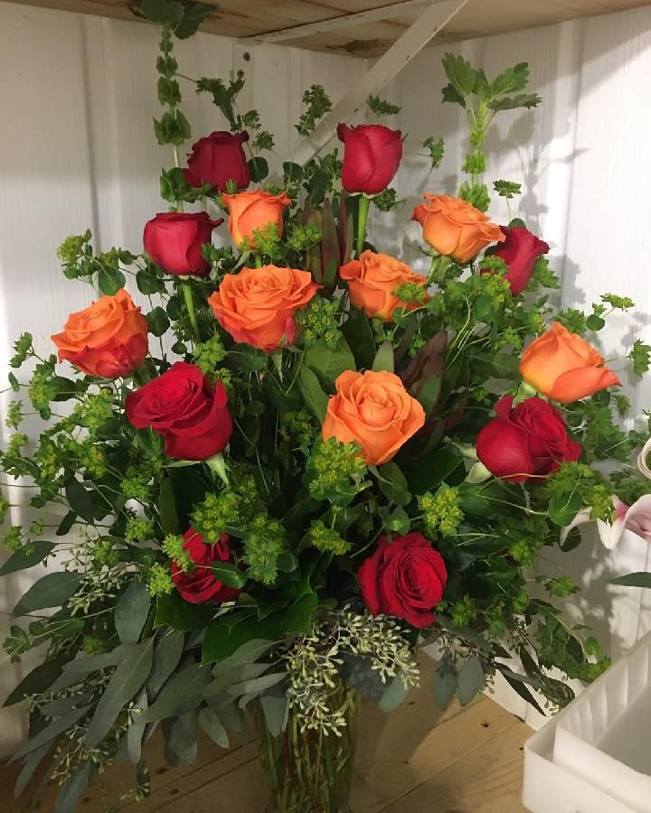 Bouquet of red and orange roses with greenery in a vase