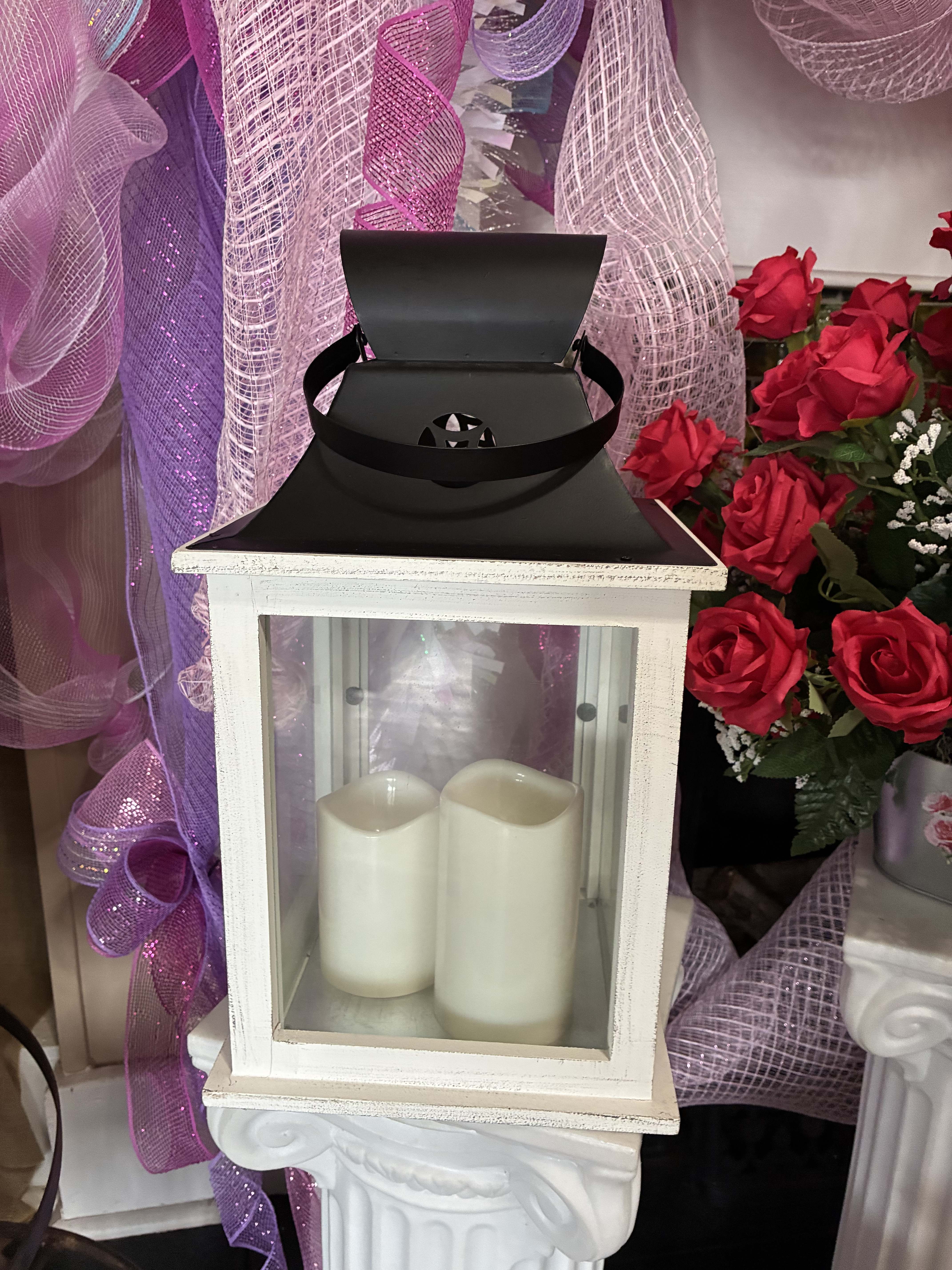 White lantern with two pillar candles beside red roses